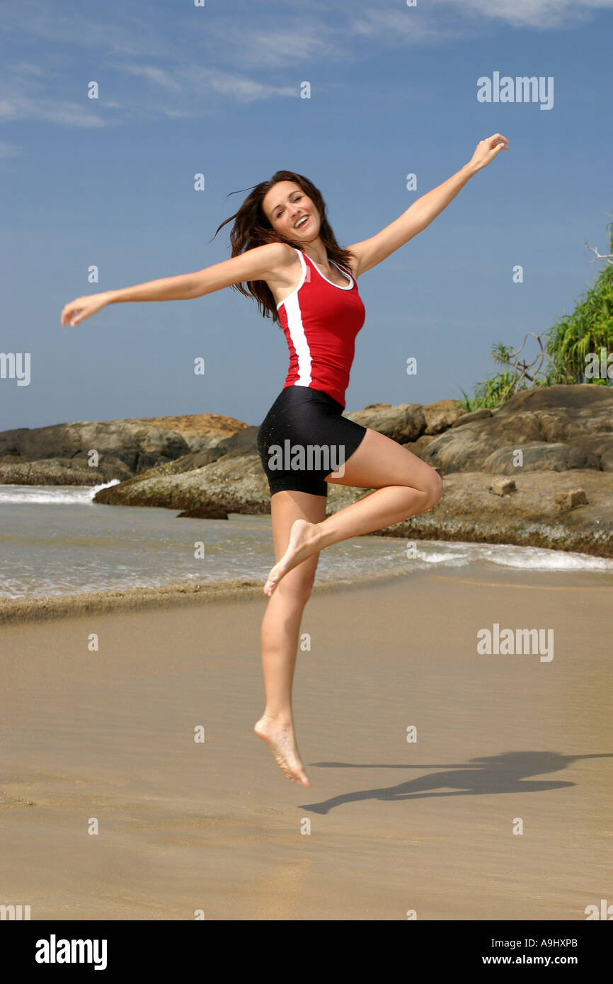 woman jumping on the beach, wearing red t-shirt and shorts. Stock Photo
