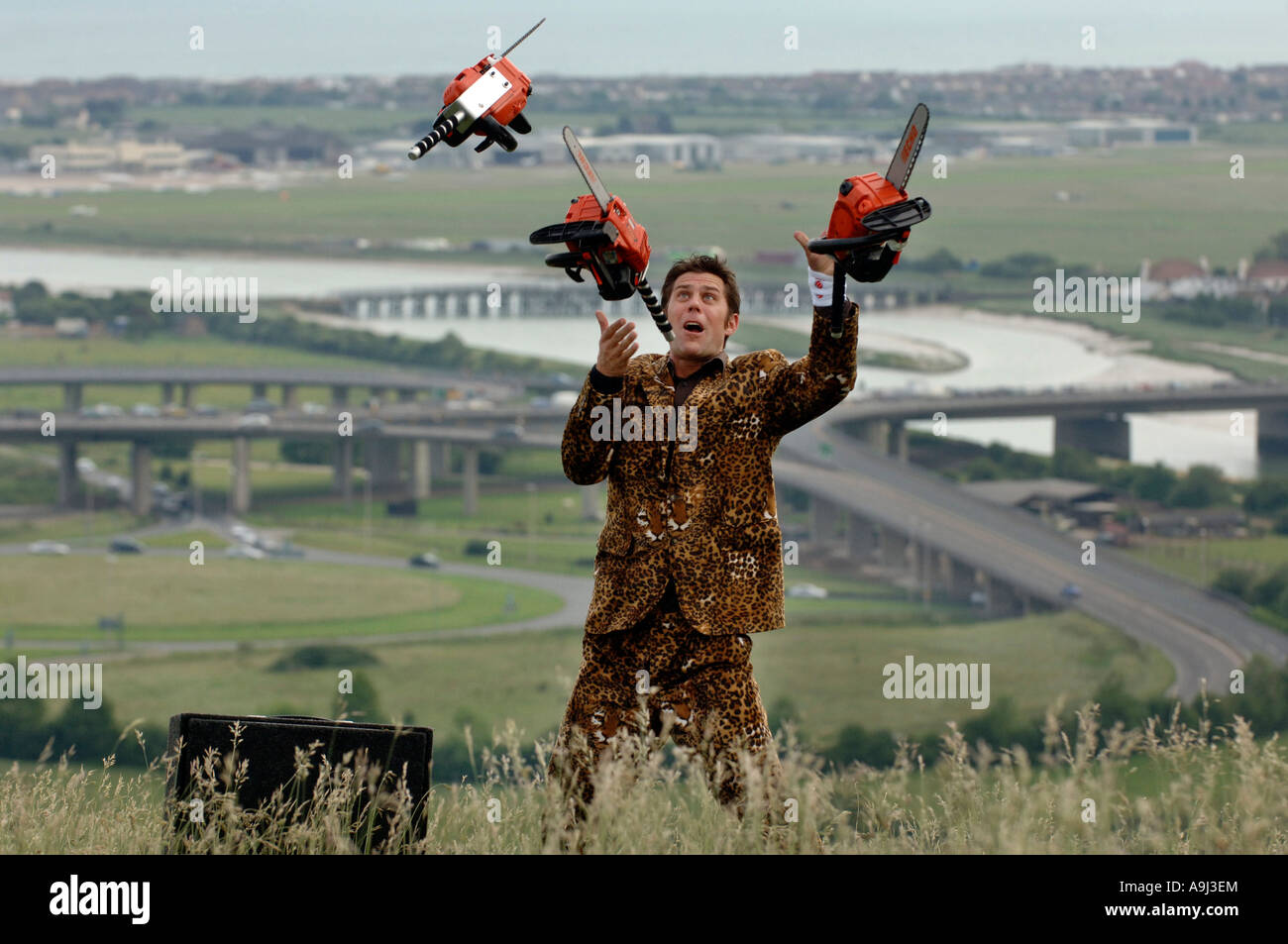 Young entertainer in leopardskin jacket juggling three orange chainsaws Stock Photo