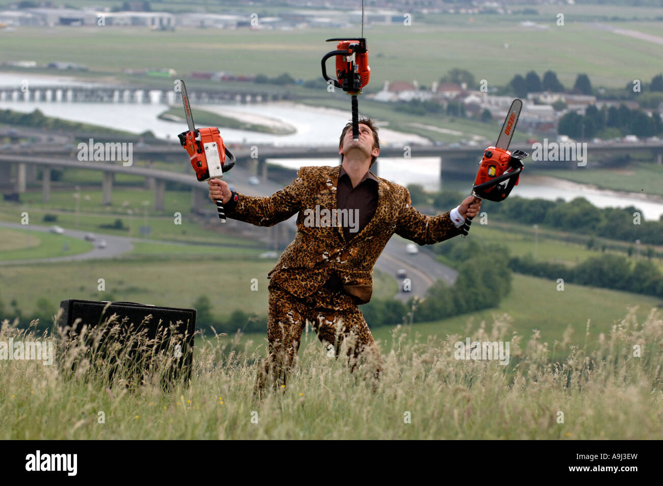 Young entertainer in leopardskin jacket juggling three orange chainsaws Stock Photo