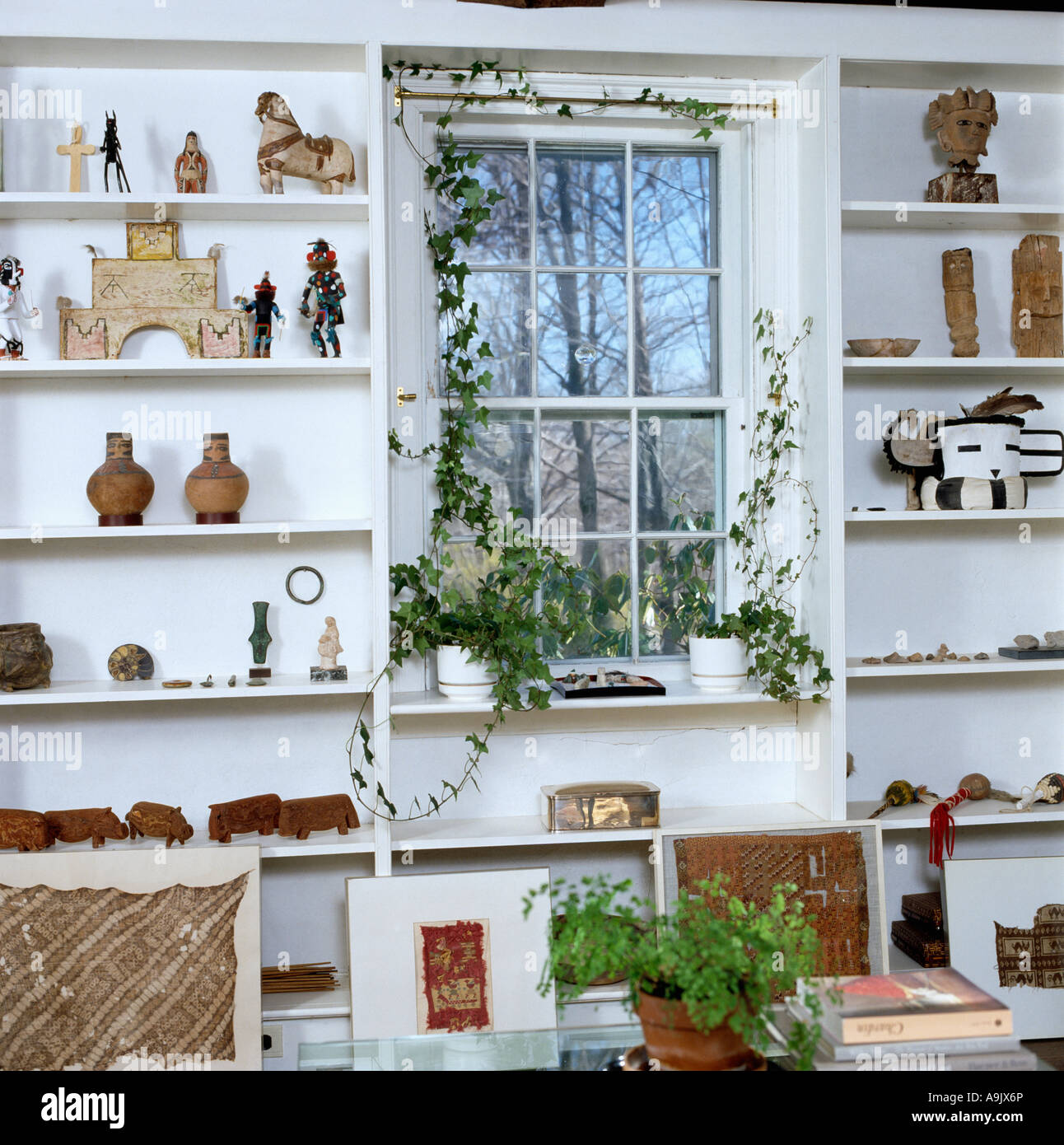 Ethnic sculpture collection on white shelves framing window with climbing ivy Stock Photo Alamy