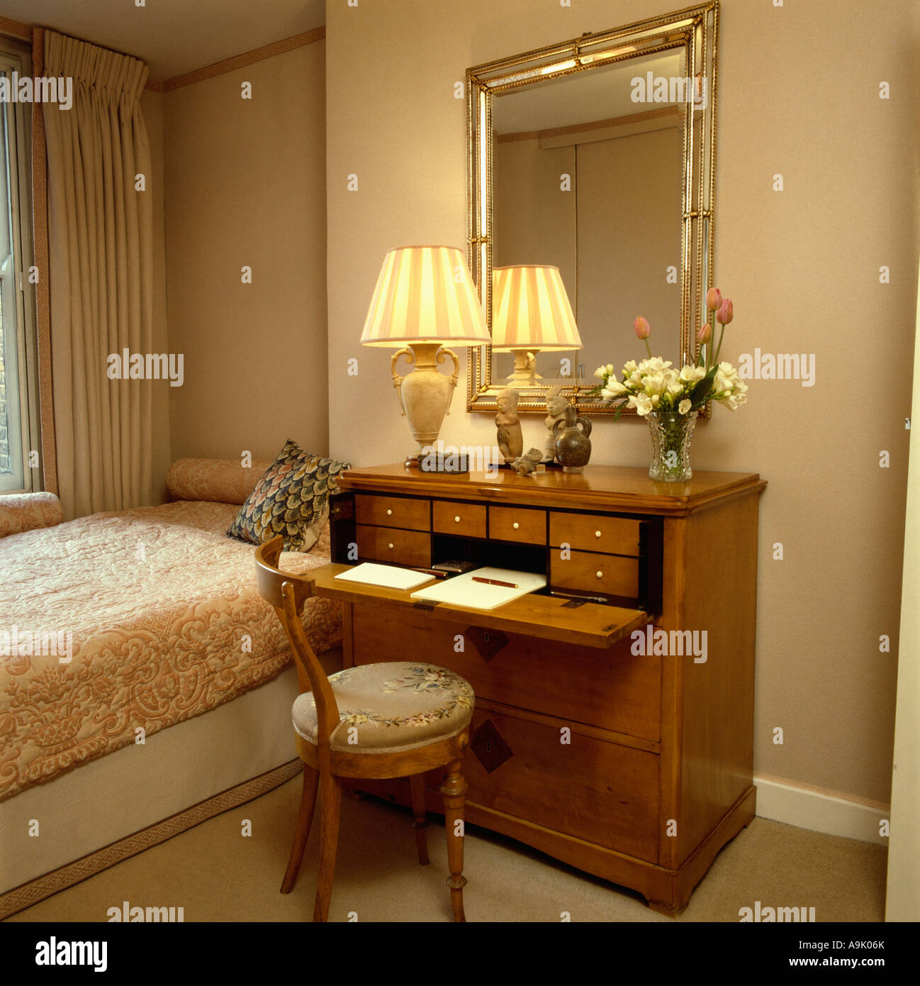 Mirror Above Antique Desk With Lighted Lamp In Neutral Guest Room