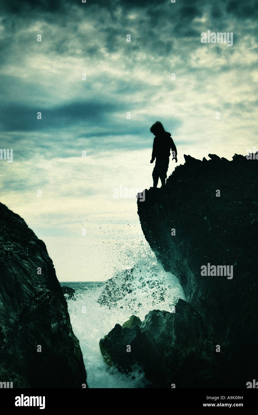 young boy stood on the edge of rocks with crashing waves Stock Photo