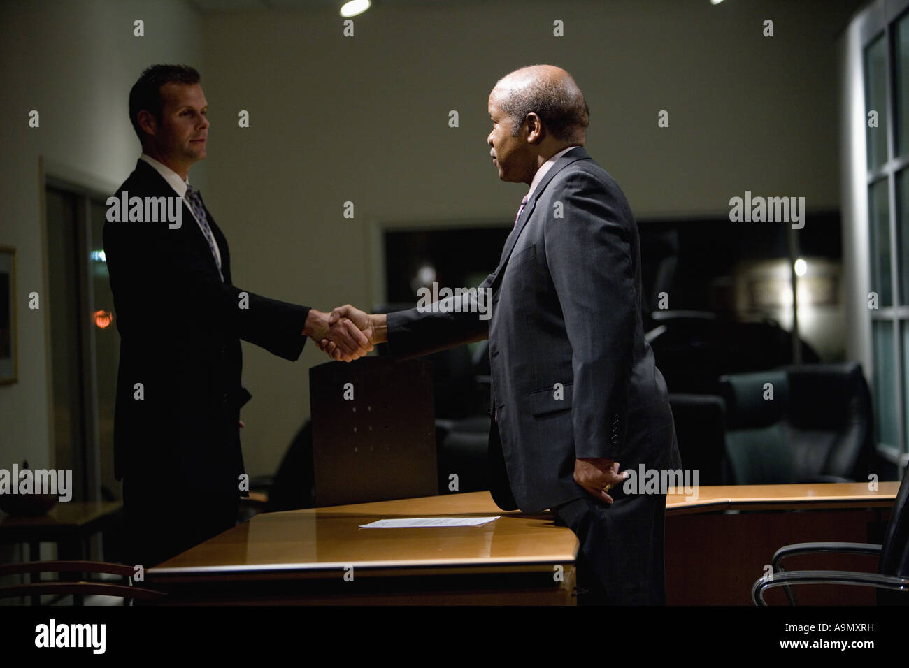 Two businessmen shaking hands across an office desk Stock Photo - Alamy