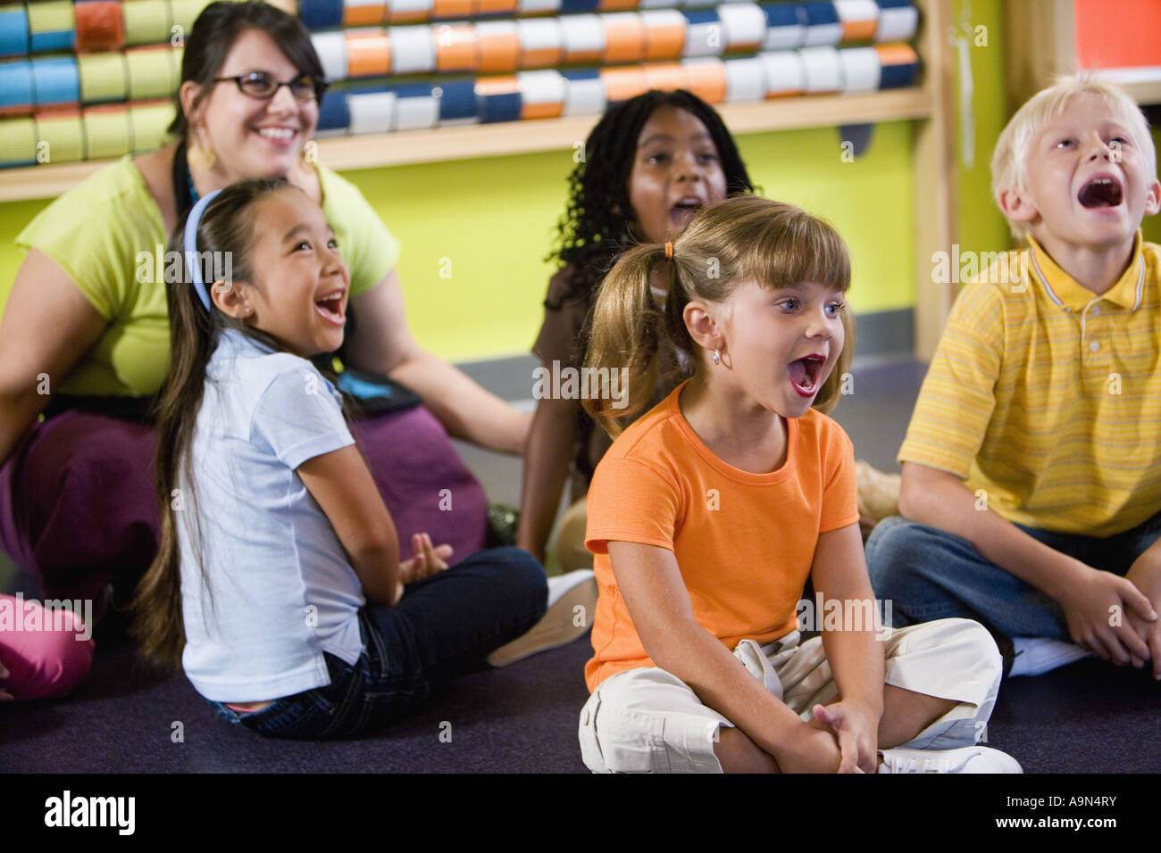Teacher sitting and posing with students in a colorful classroom Stock ...