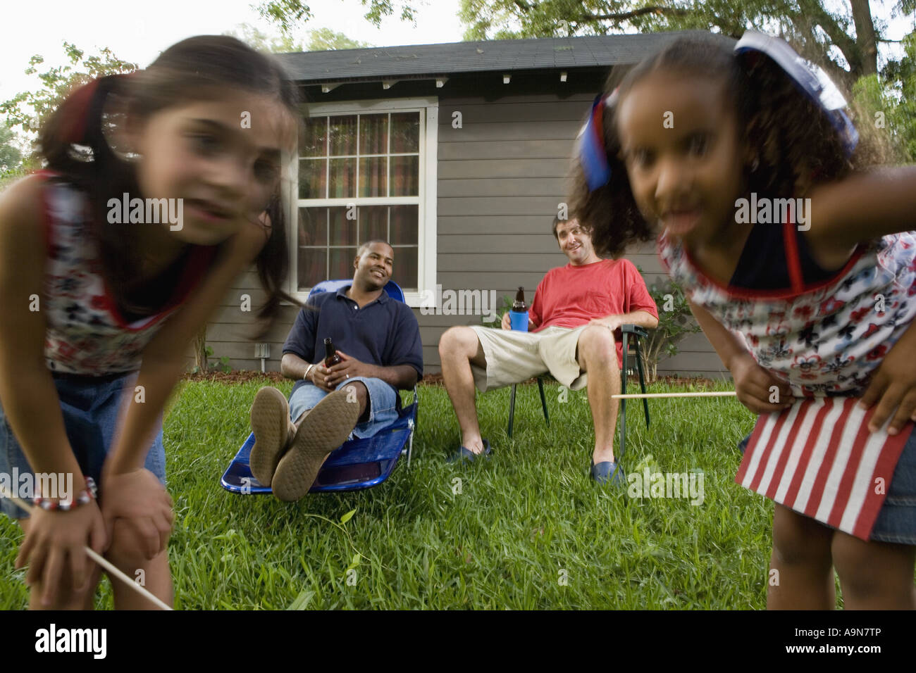 Two young men sitting on lawn chairs enjoying a beer while daughters