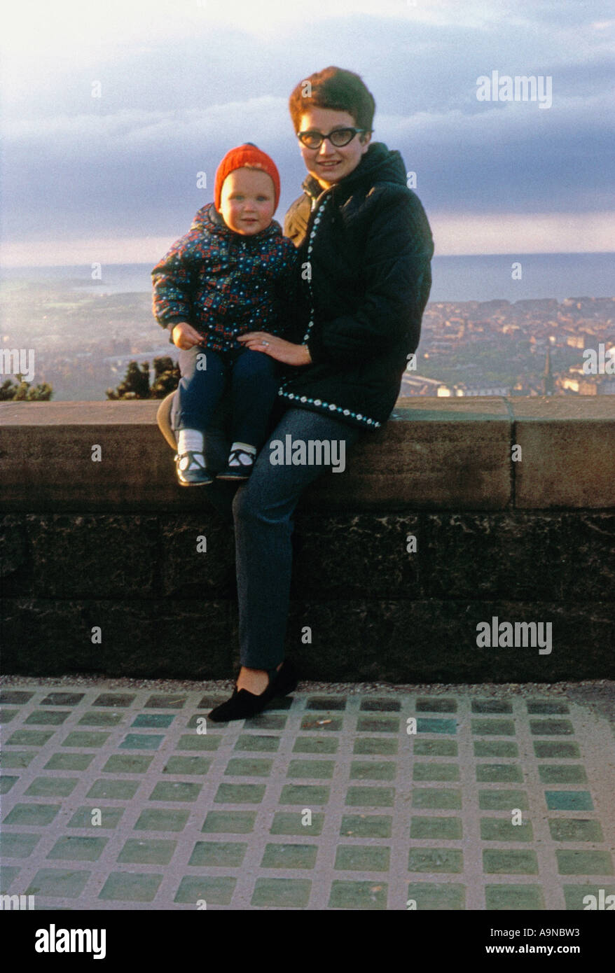 Young Caucasian woman and small child posing on the wall of Oliver's Mount with Scarborough and the North Sea in the distance circa1960. Stock Photo