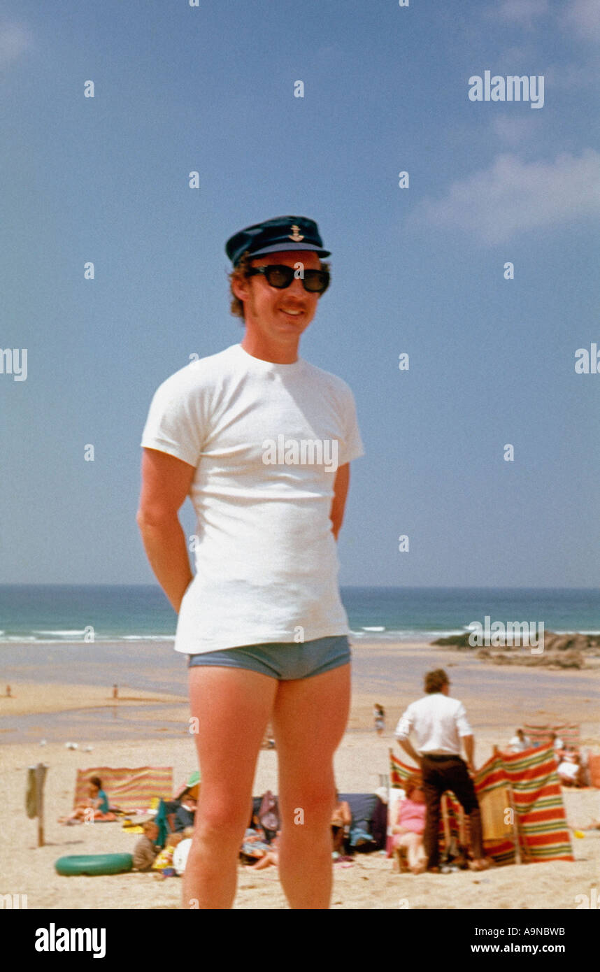 Young Caucasian man in a peaked sailor cap, white t-shirt, and swimming trunks on the beach, 1960s. Archive photo Stock Photo