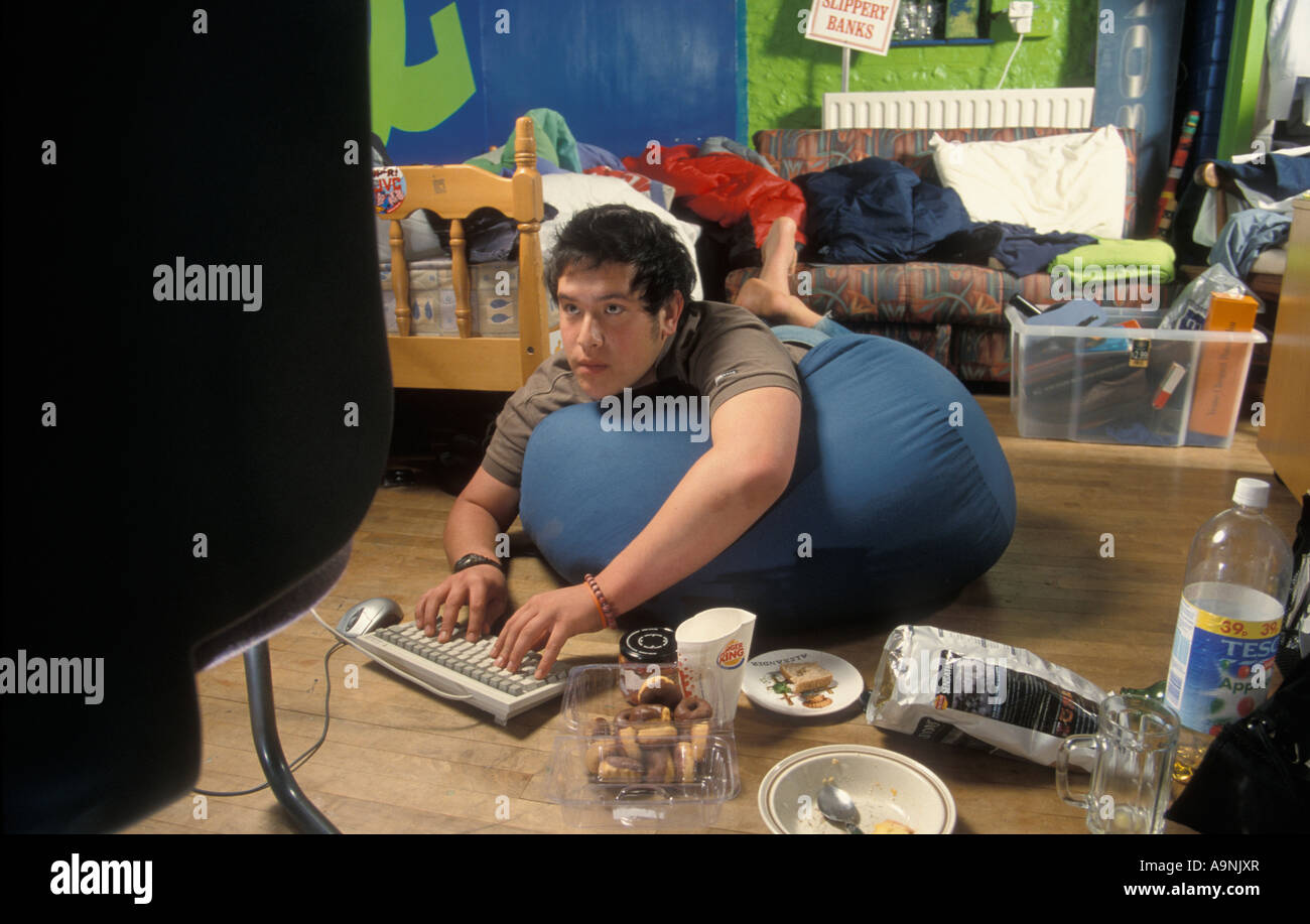 teenage boy computer nerd playing on computer in messy room surrounded by junk food Stock Photo