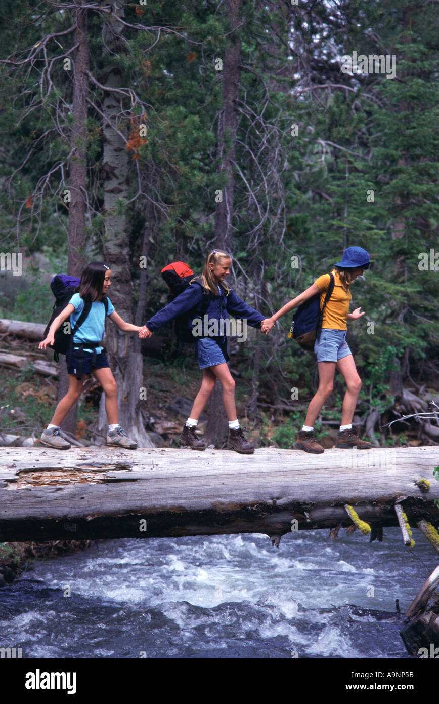 Three young girls crossing a log over Prosser Creek CA Stock Photo