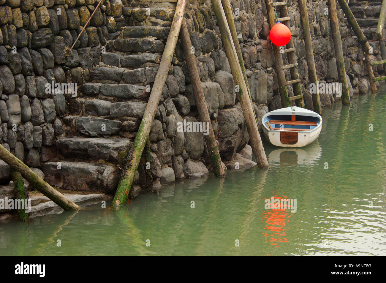 Small white dinghy and bright orange buoy secured to the historic 14th century stone built harbour wall at Clovelly North Devon Stock Photo