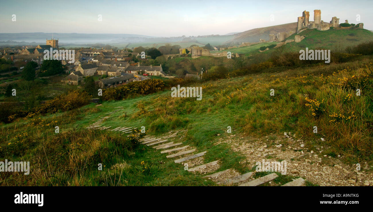 Derelict castle and village of Corfe Castle in early morning light and a clear sky with steps leading down the hill Stock Photo