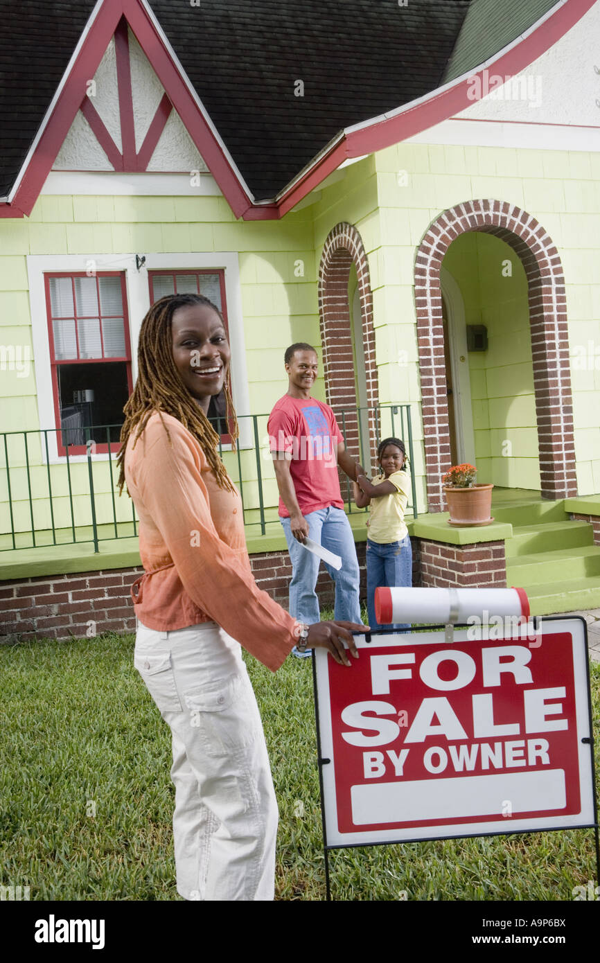 Family outside house with woman standing by "For Sale" sign Stock Photo ...
