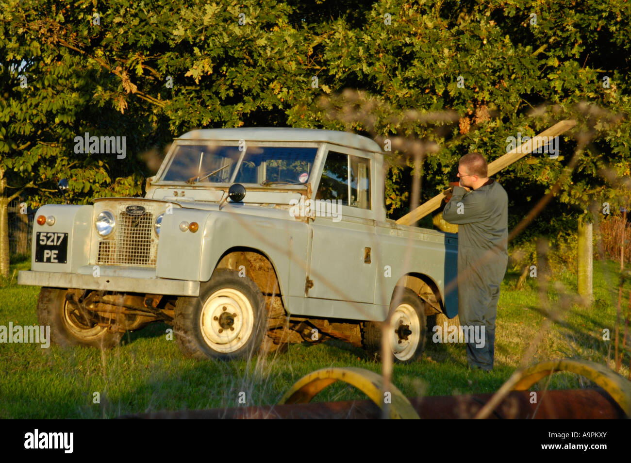 Farmer in overall loading timber into an old 1960 s Landrover Series 2a short wheel base truckcab. Stock Photo