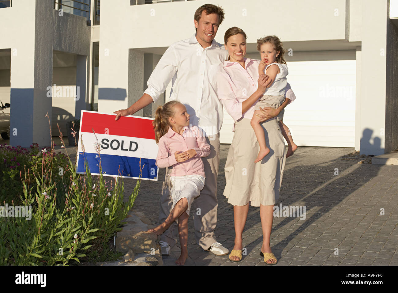 Family stood outside house holding sold sign Stock Photo - Alamy