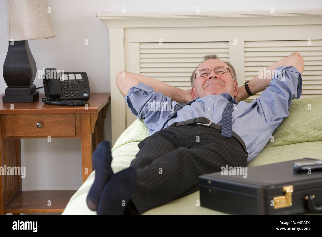 Businessman laying on bed in hotel room Stock Photo