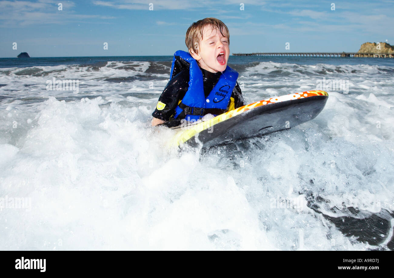 boy 6 playing in the surf on body boogie board wearing wet suit and