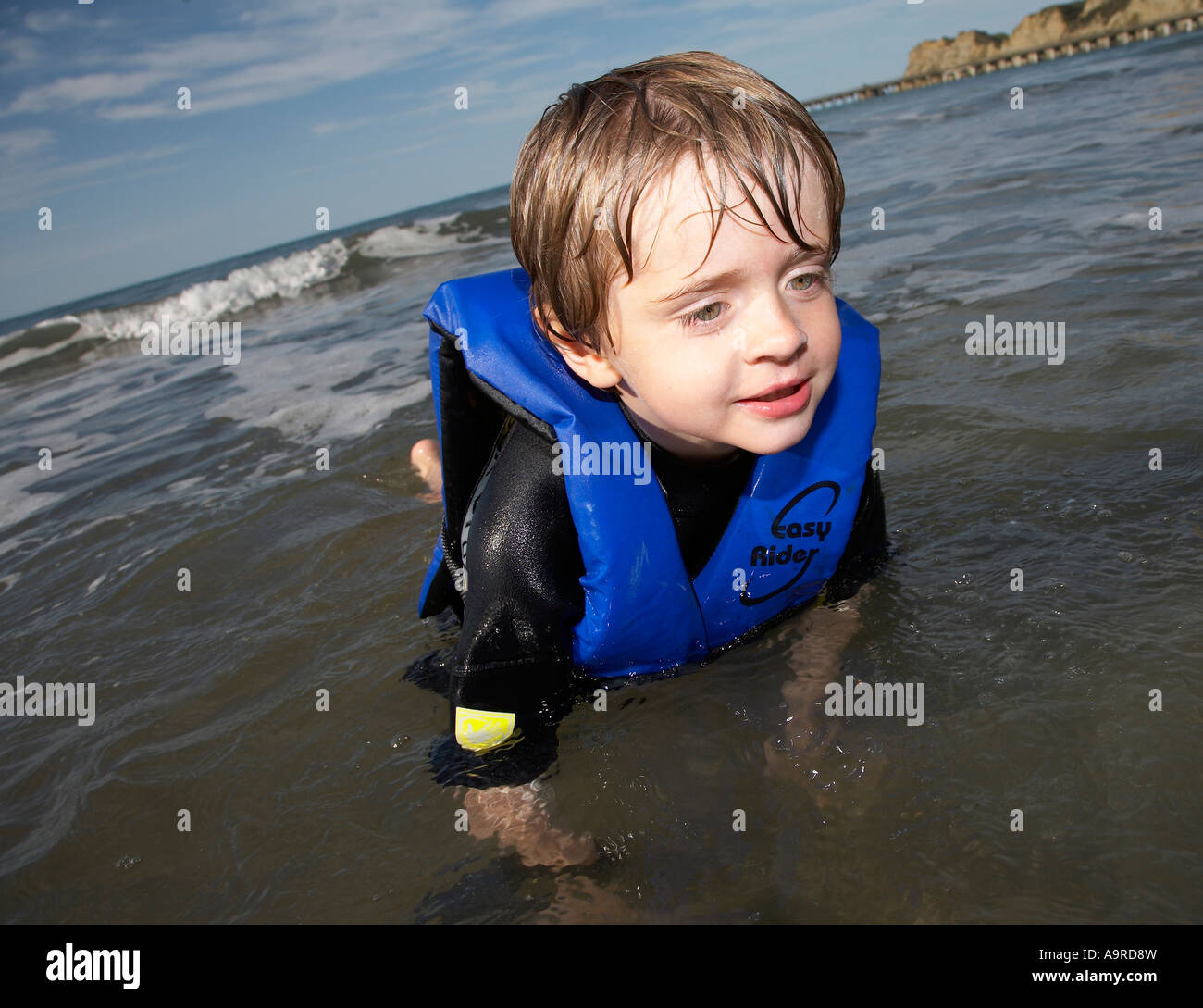 boy playing in the water wearing wetsuit and life jacket Stock Photo