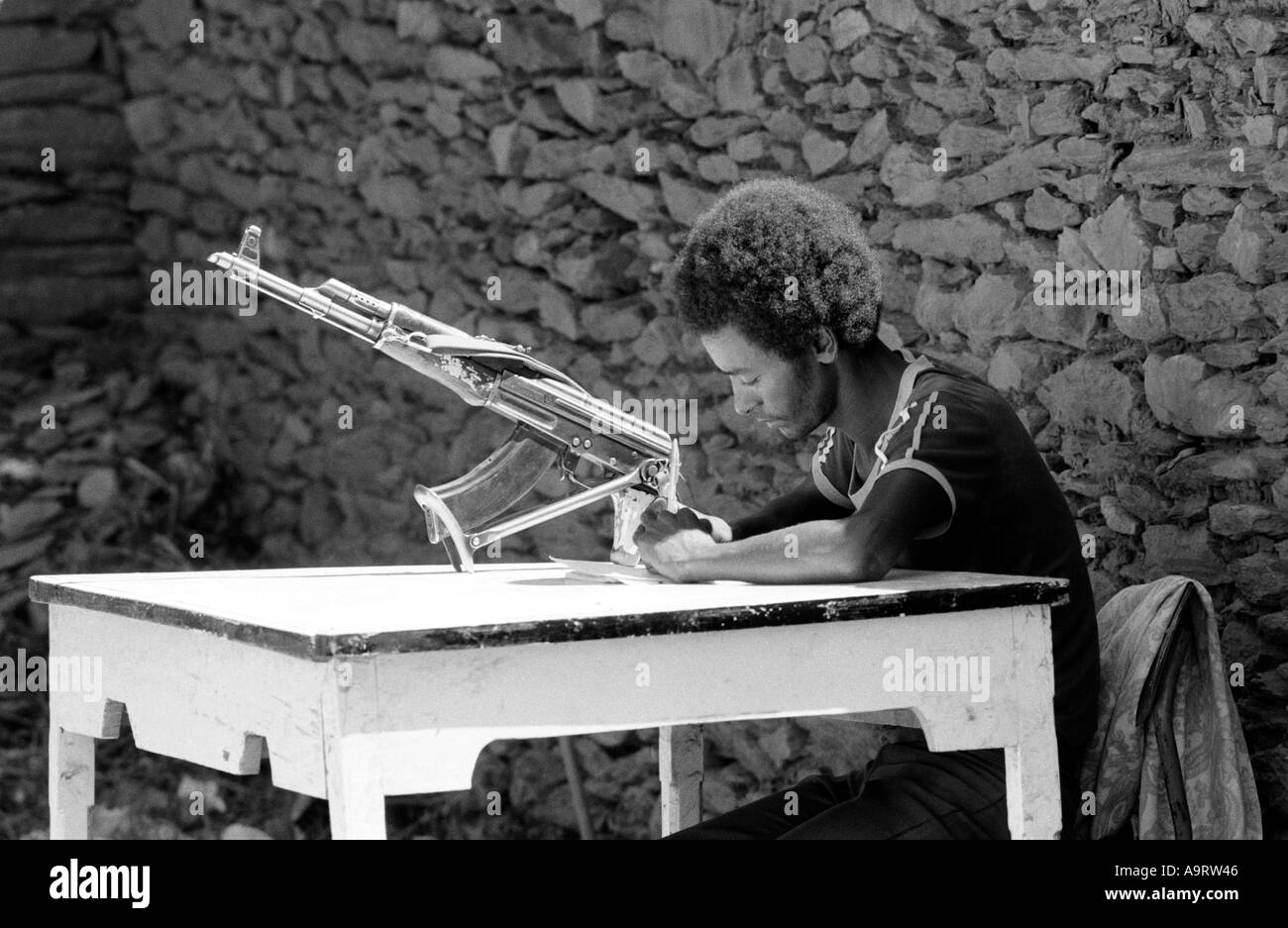 B/W of a TPLF fighter in casual clothes with kalashnikov, sitting at a table, writing home during the civil war. Tigray, Ethiopia Stock Photo