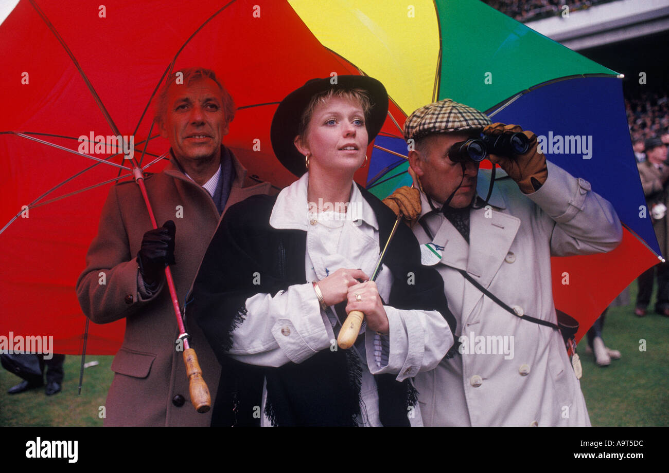 Cheltenham Festival horse racing 1990s UK. Cheltenham Gold Cup race goers sheltering under colourful umbrella. Gloucestershire England HOMER SYKES Stock Photo