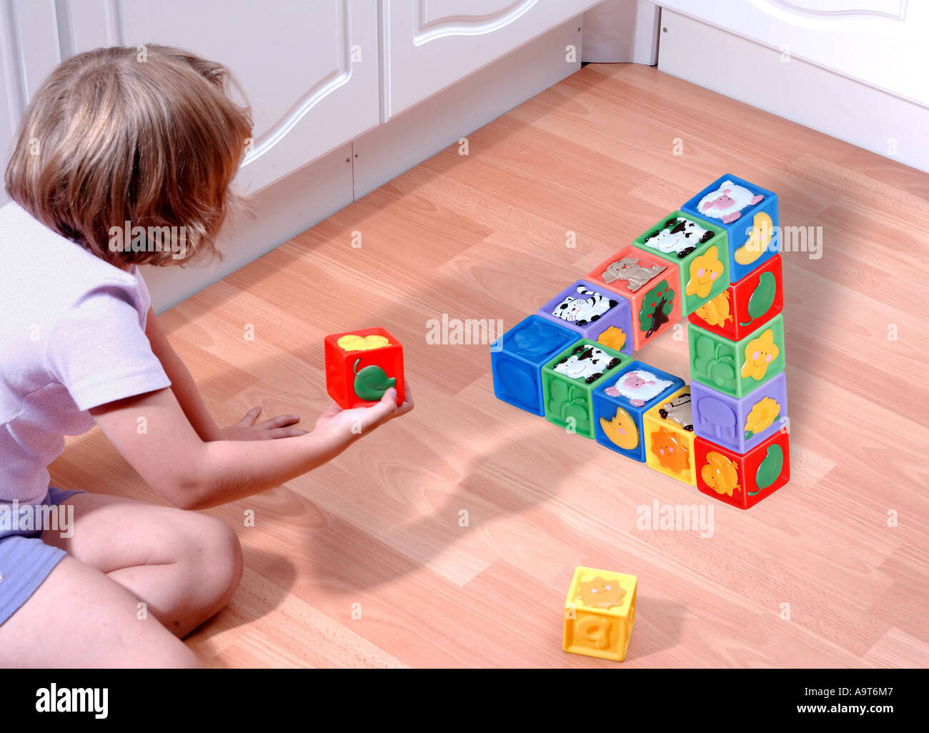Child playing with childrens building blocks on the kitchen floor to produce an impossible structure. Stock Photo