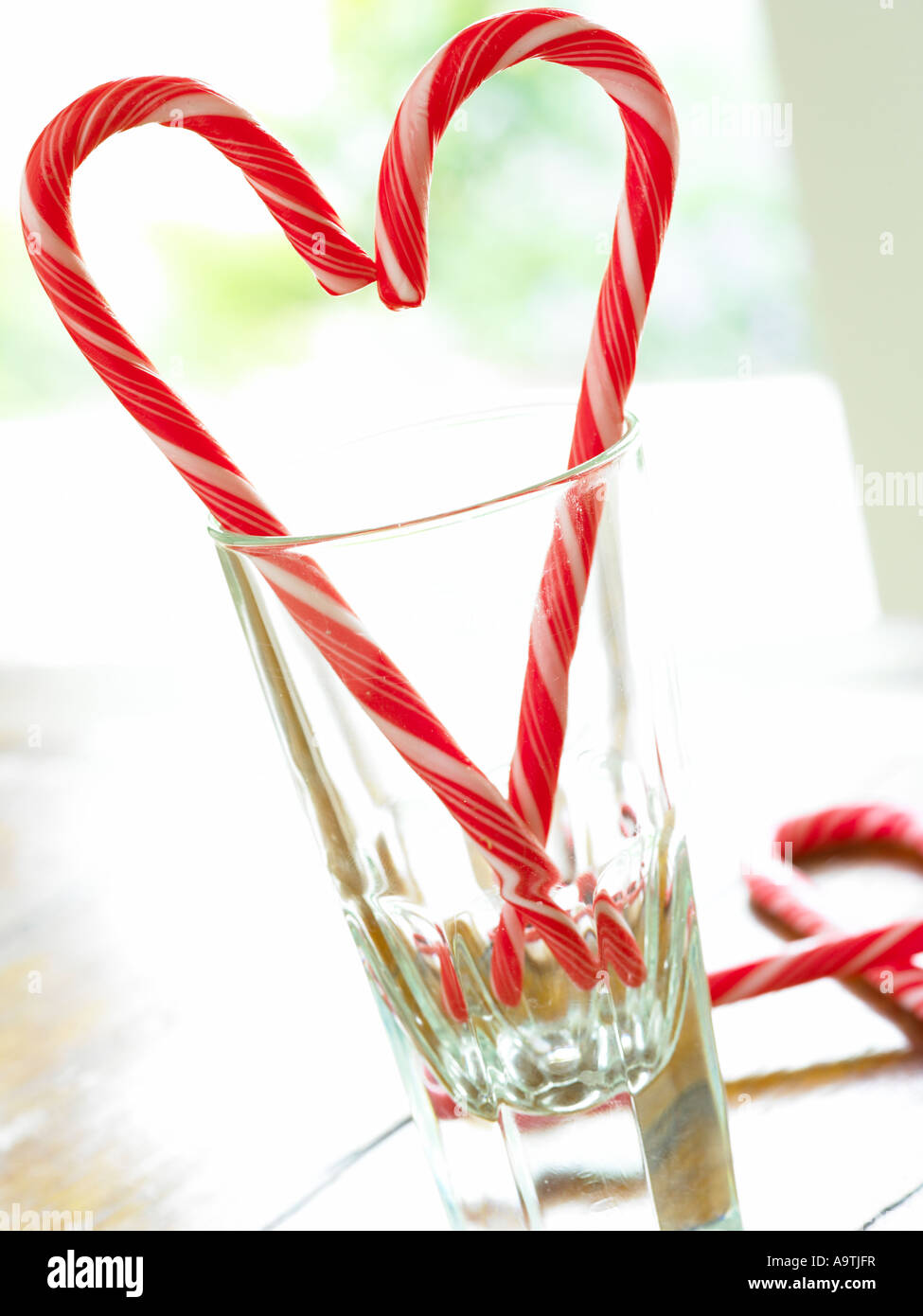 red and white candy cane sticks making a symbol of a hart shape in a glass tumbler backlit by window light Stock Photo