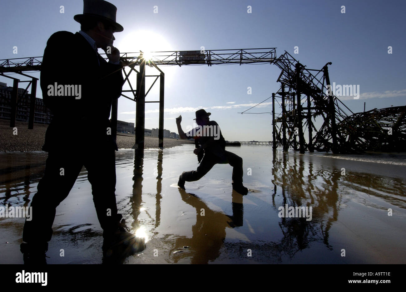 Stone skimming competition on Brighton Beach. A contender lobs a stone, watched by a judge in a top hat Stock Photo