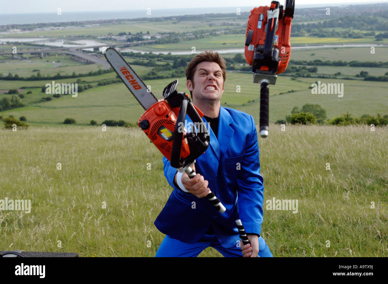 Young entertainer in blue suit juggling three orange chainsaws Stock Photo