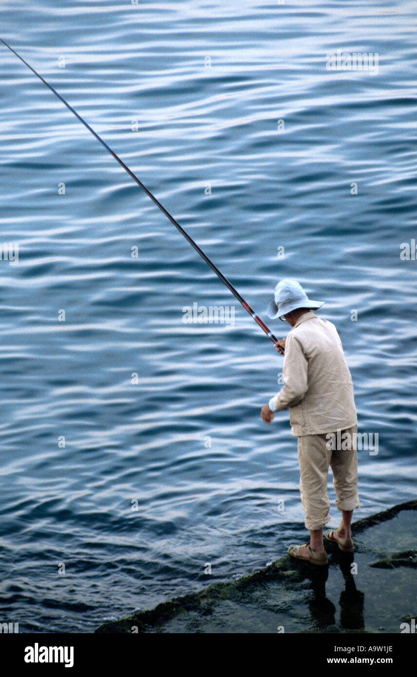 An angler on the corniche in Beirut waits for a bite in the early morning light. Stock Photo