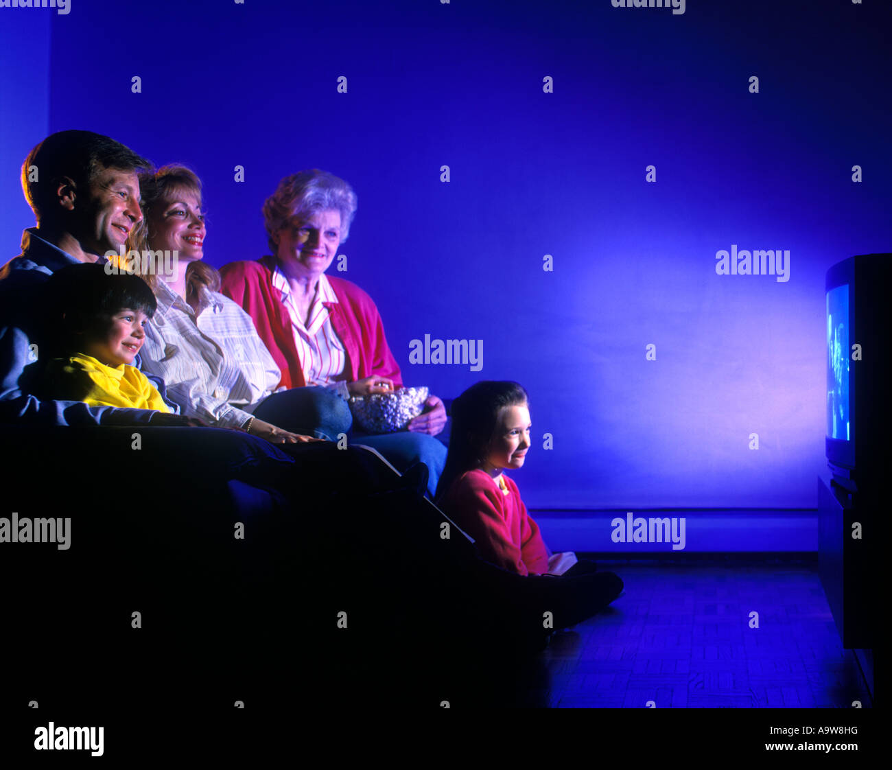 1994 HISTORICAL CAUCASIAN THREE GENERATION FAMILY SITTING ON COUCH WATCHING TELEVISION Stock Photo