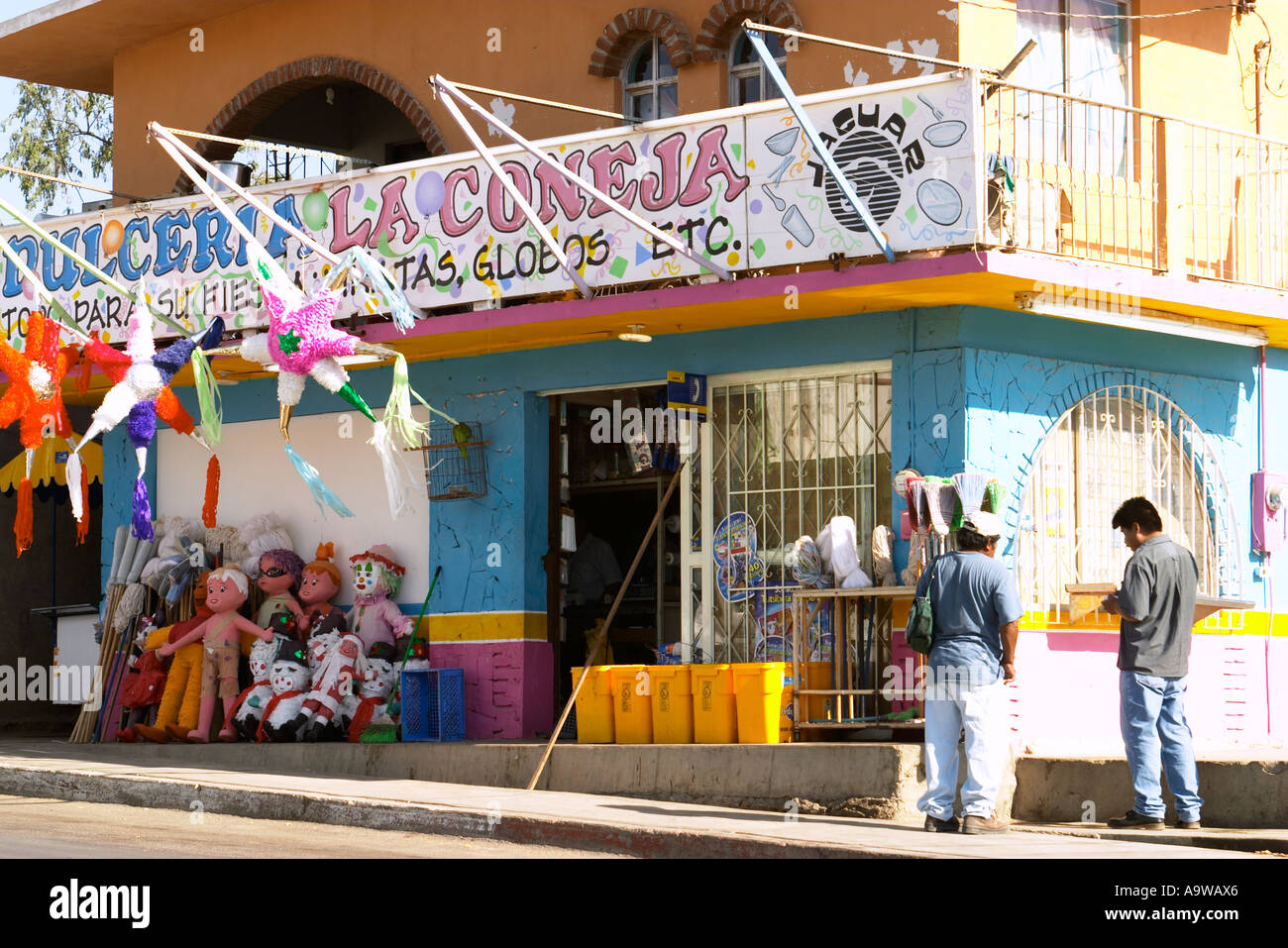 MEXICO Cabo San Lucas Two men stand outside party store colorfuly blown up plastic figures pinatas Stock Photo