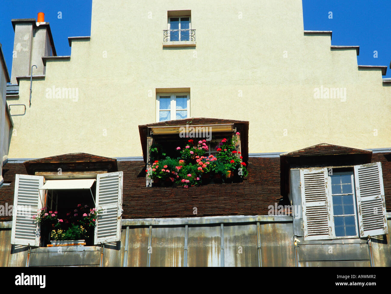 Paris architecture: Stepped roof, or rooftop, of a white house. Dutch influence. Open shutters and a window box with red and pink flowers. Stock Photo