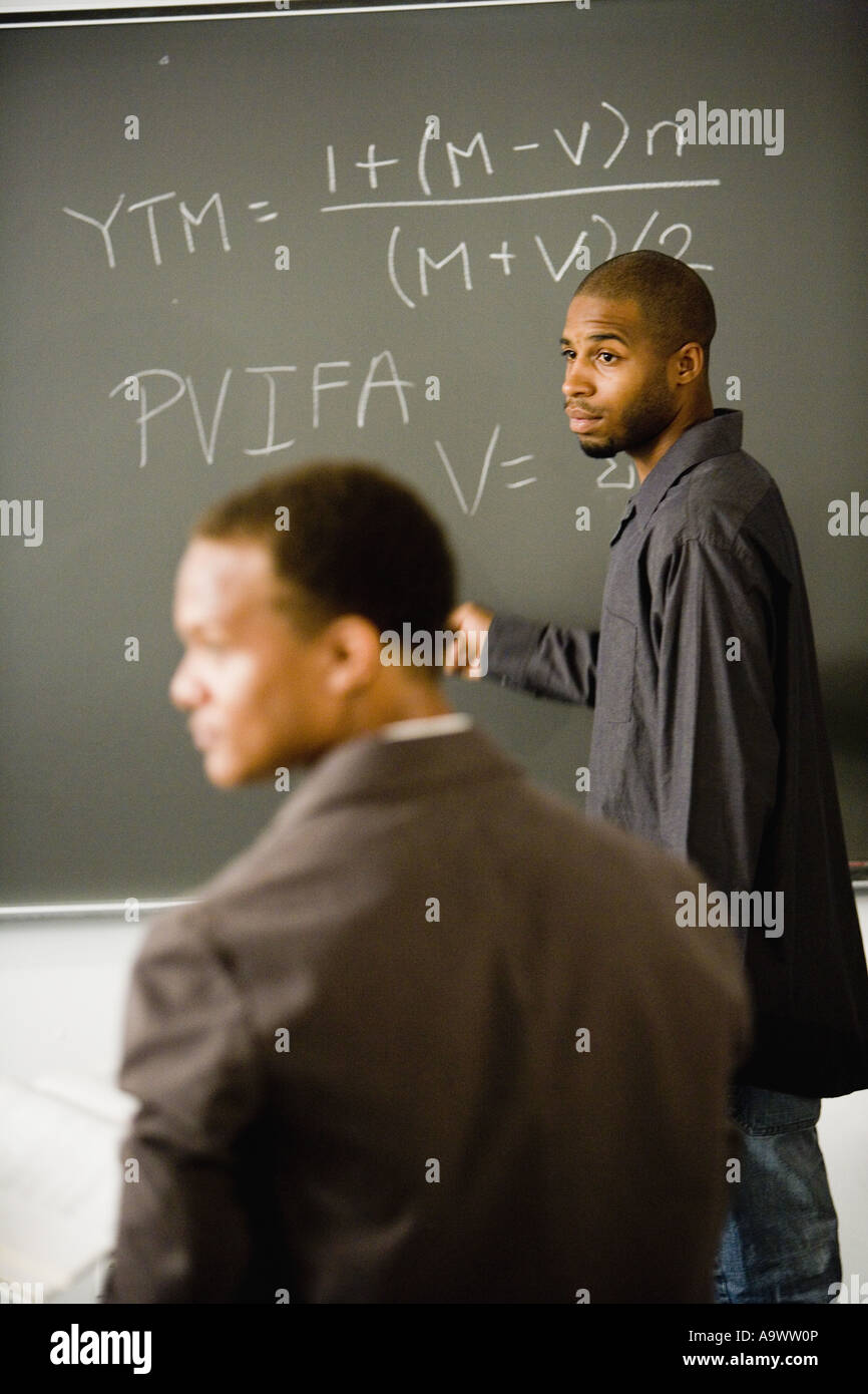 Student writing on the chalkboard in front of teacher Stock Photo - Alamy