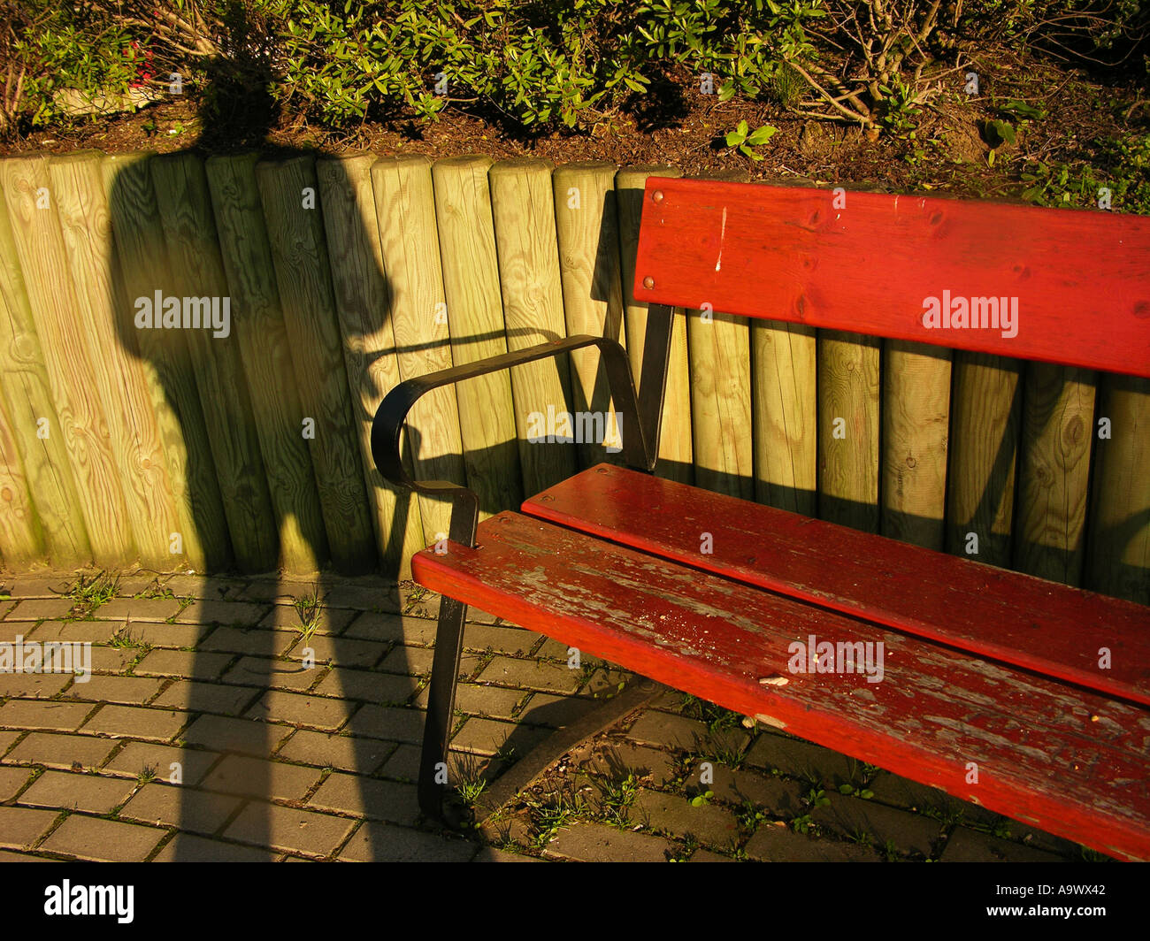 Shadow of a man standing next to a red park bench Stock Photo