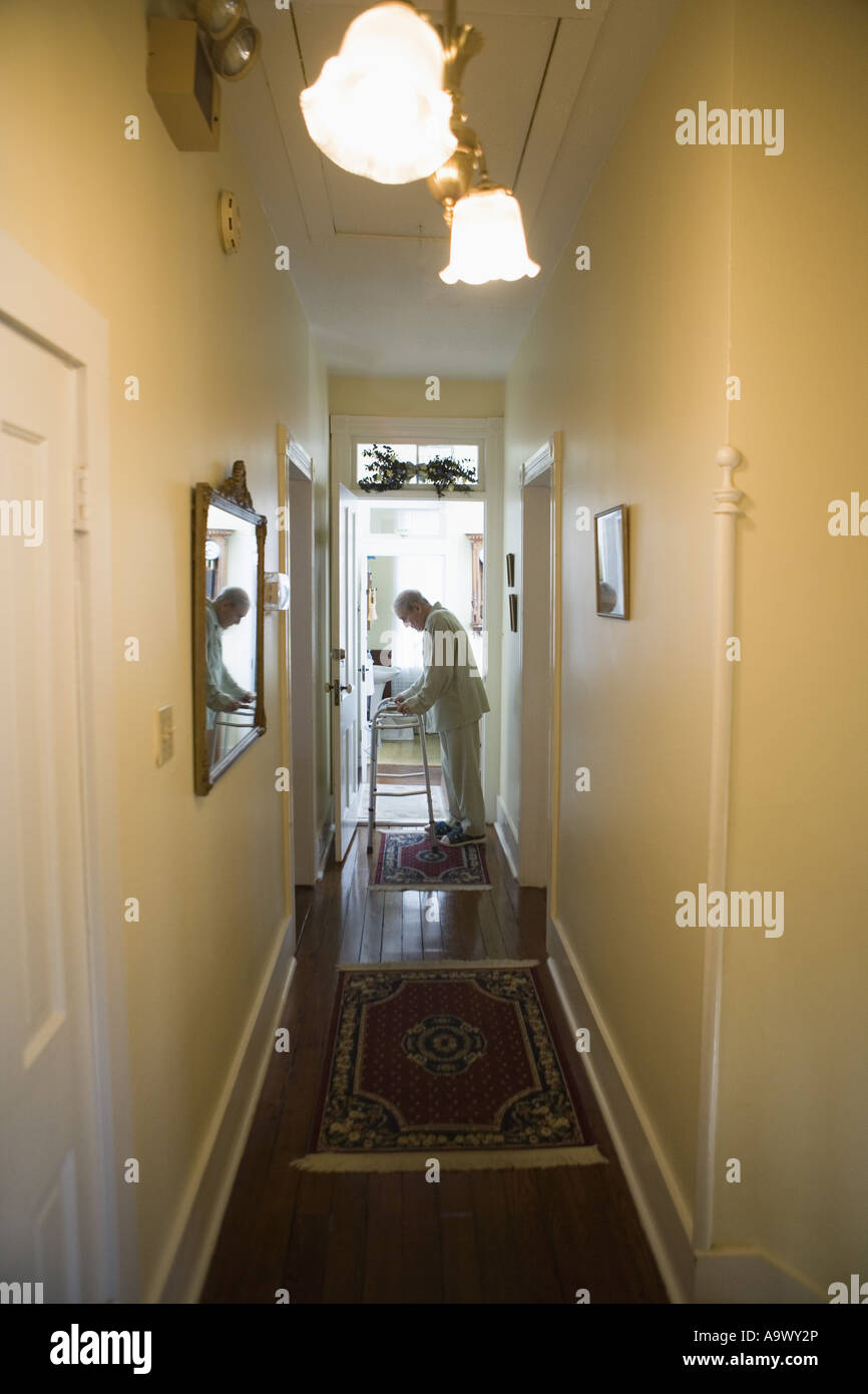 Feeble senior man slowly going down hallway with walker Stock Photo