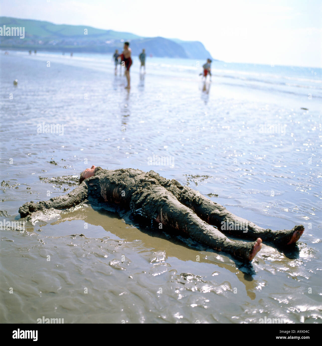 A man lying belly up collapsed on a sandy beach covered in sand Borth, Ceredigion Wales UK Stock Photo