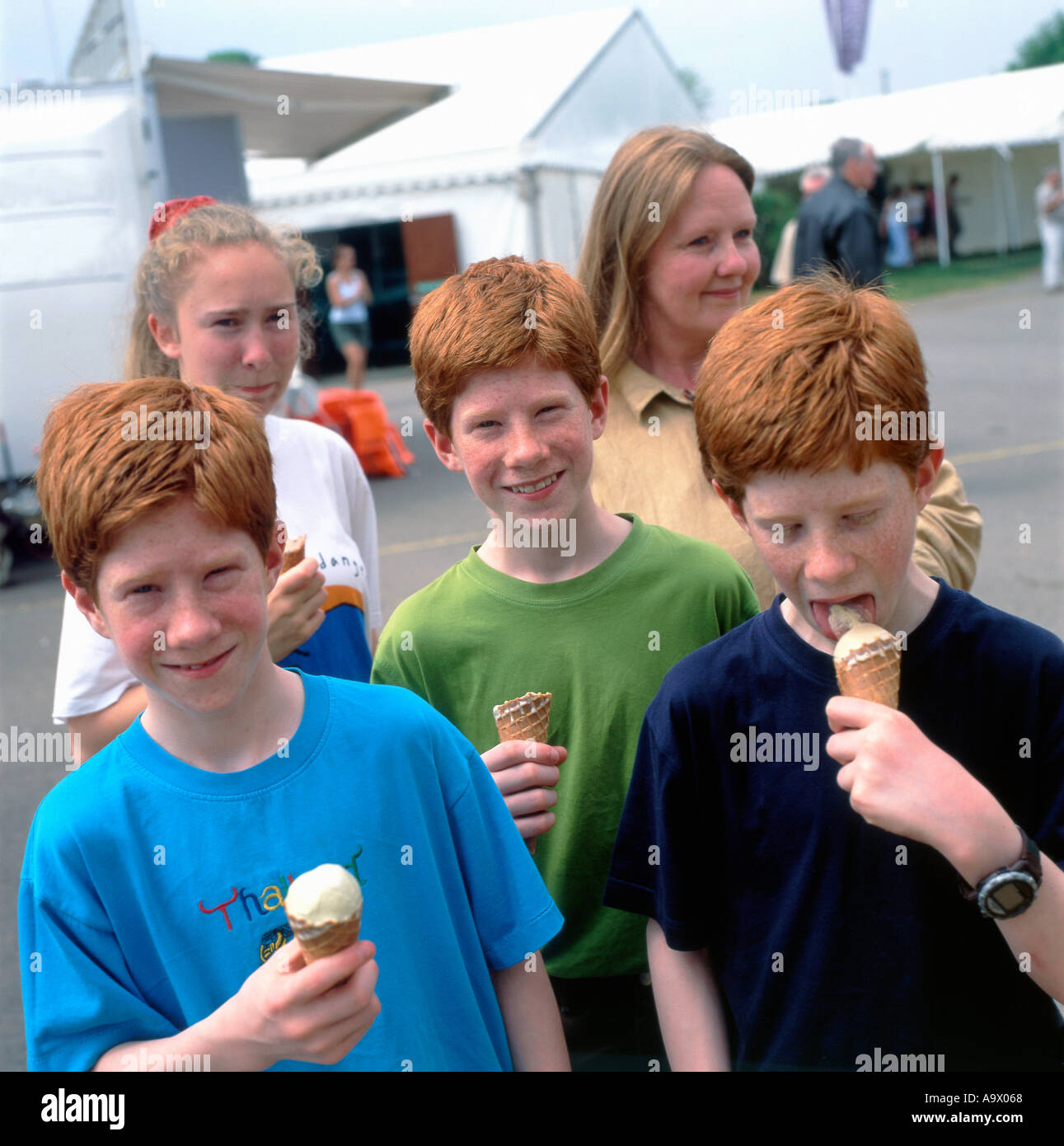 A family with identical genes ginger hair triplet boys 12 or 13 years kids children eating ice cream in Britain UK  KATHY DEWITT Stock Photo