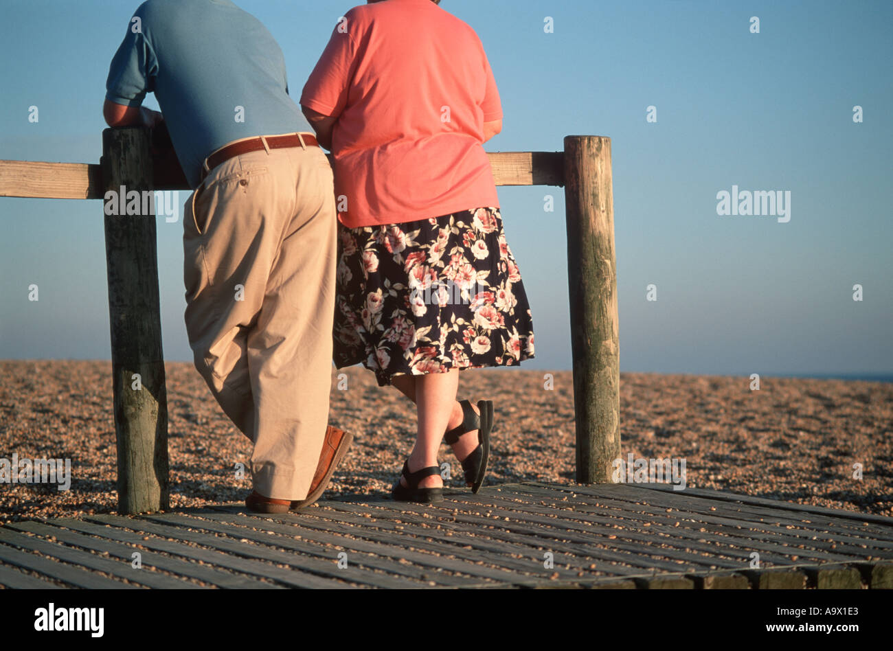 Resting On Railing Senior couple resting against railing looking across shingle beach low ...