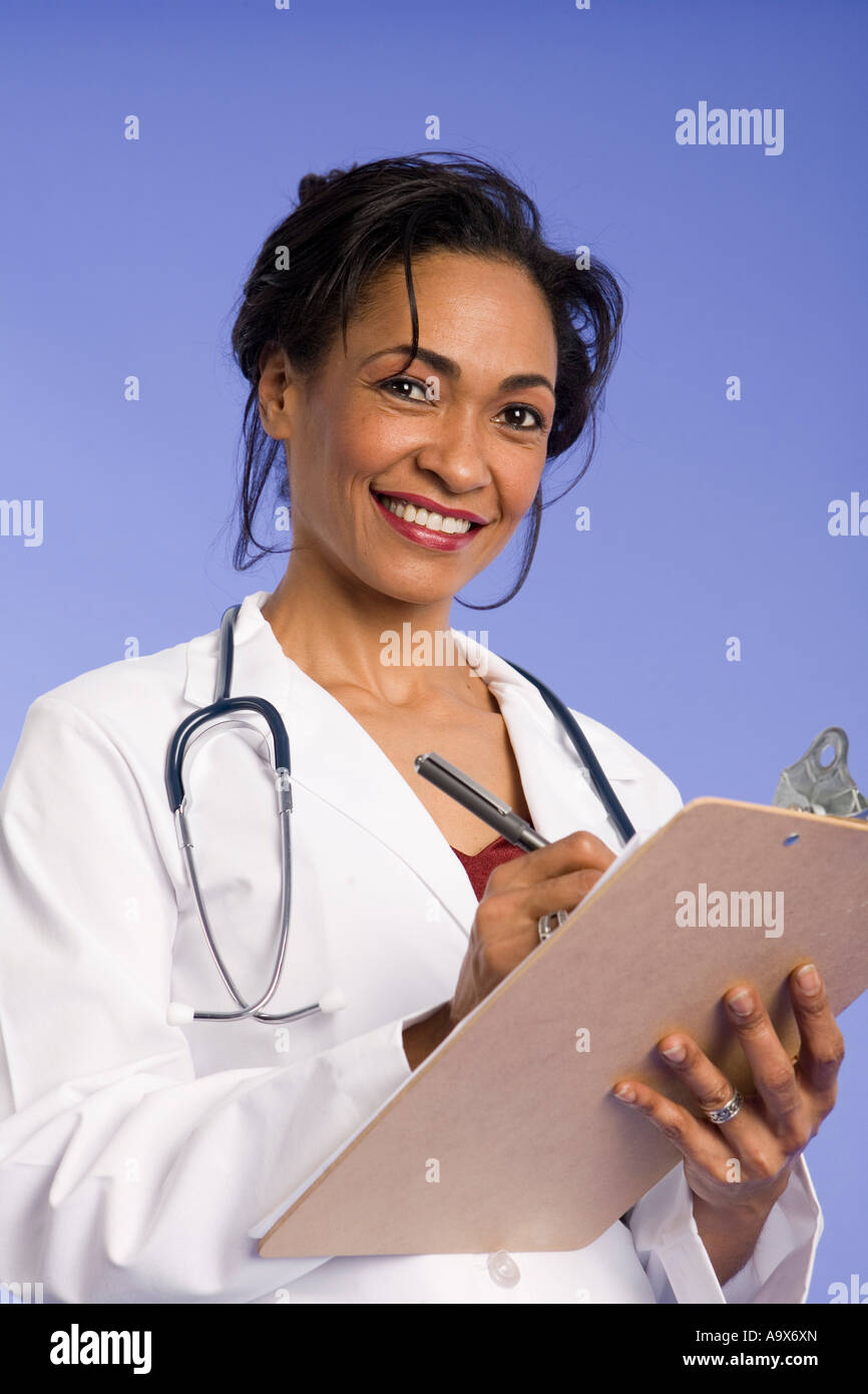 Smiling female doctor in a white coat writing on a clip board wearing a