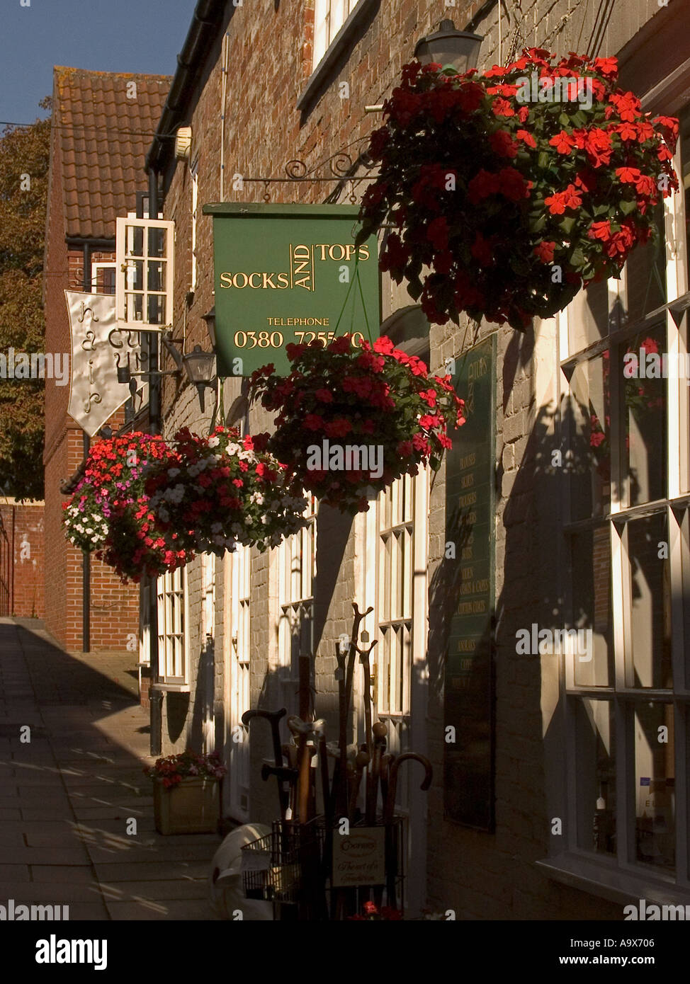 Hanging baskets filled with red flowers above shopfronts, white painshopfronts, alleyway The Ginney  off Market Place, Devizes, Wiltshire, England, UK Stock Photo
