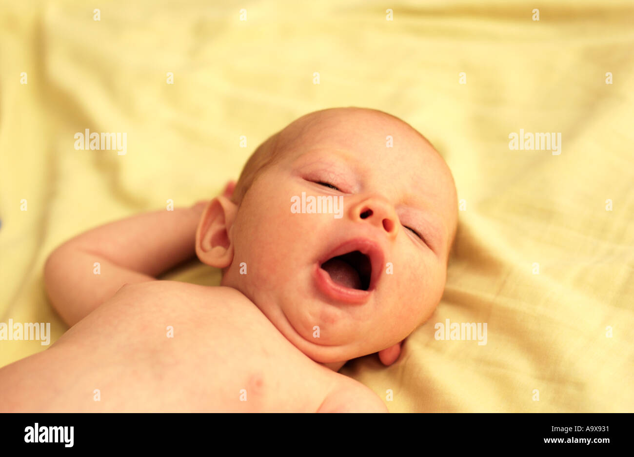 Baby lying on yellow blanket yawning Stock Photo