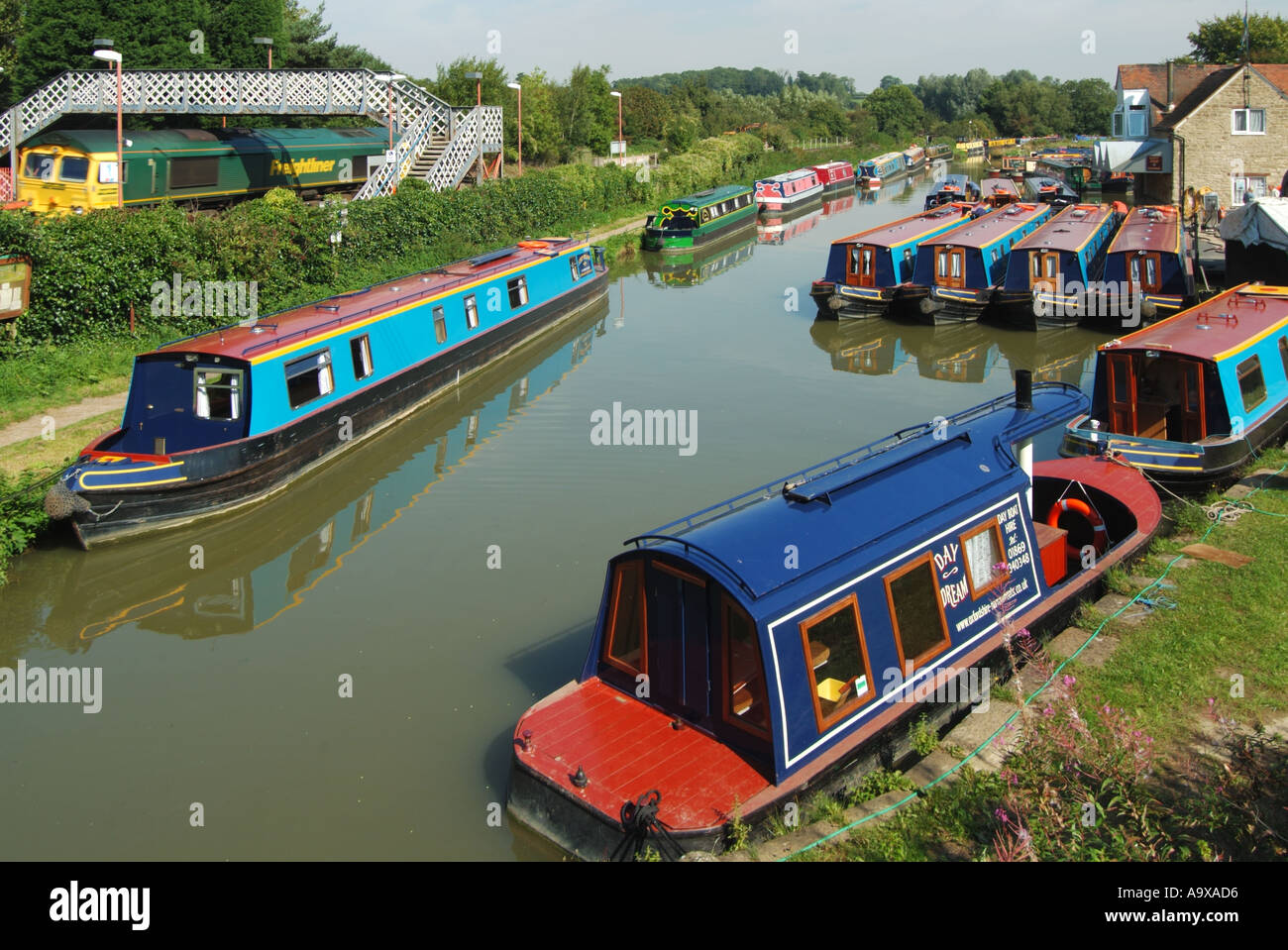 Lower Heyford train station freightliner locomotive & footbridge compare narrowboat pleasure use on old Oxford Canal built for freight Oxfordshire UK Stock Photo
