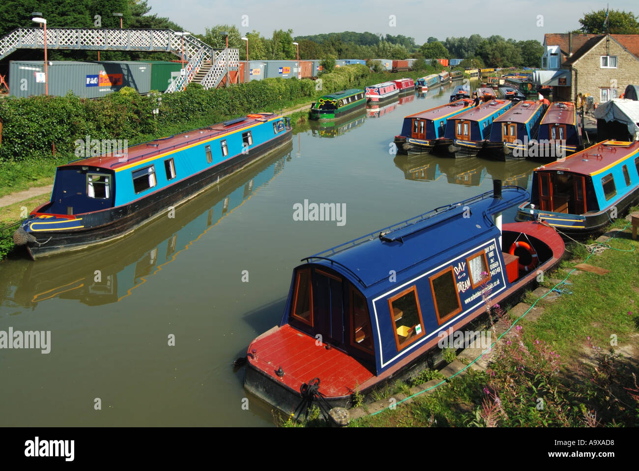 Lower Heyford station shipping container freight train & footbridge compare narrowboat pleasure use on old Oxford Canal built for cargo Oxfordshire UK Stock Photo