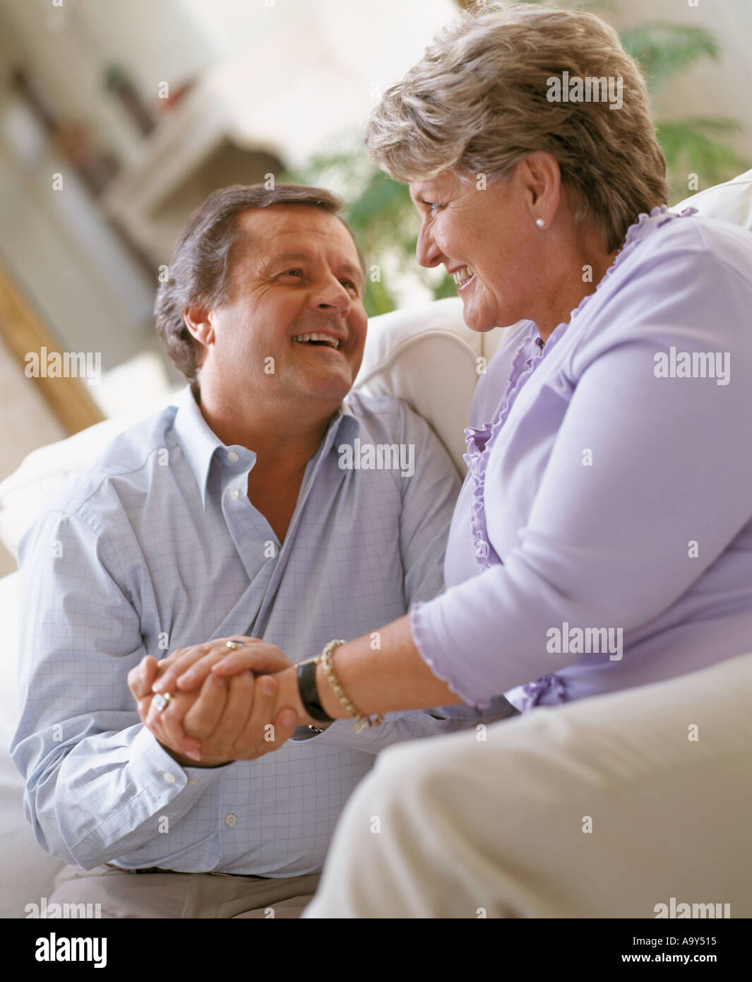 middle aged couple laughing and holding hands on sofa Stock Photo