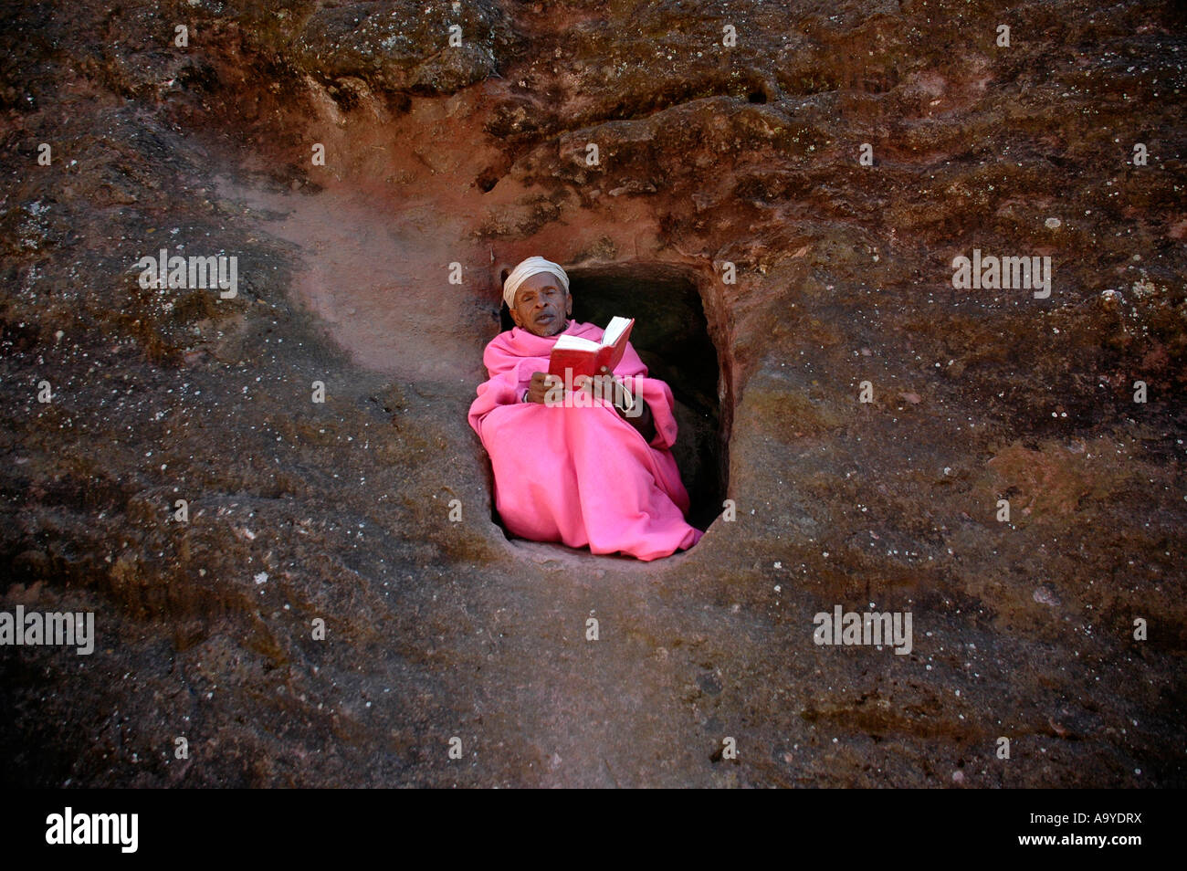 Hermit dressed in a pink cape praying in a small rock cave rock curches Lalibela Ethiopia Stock Photo