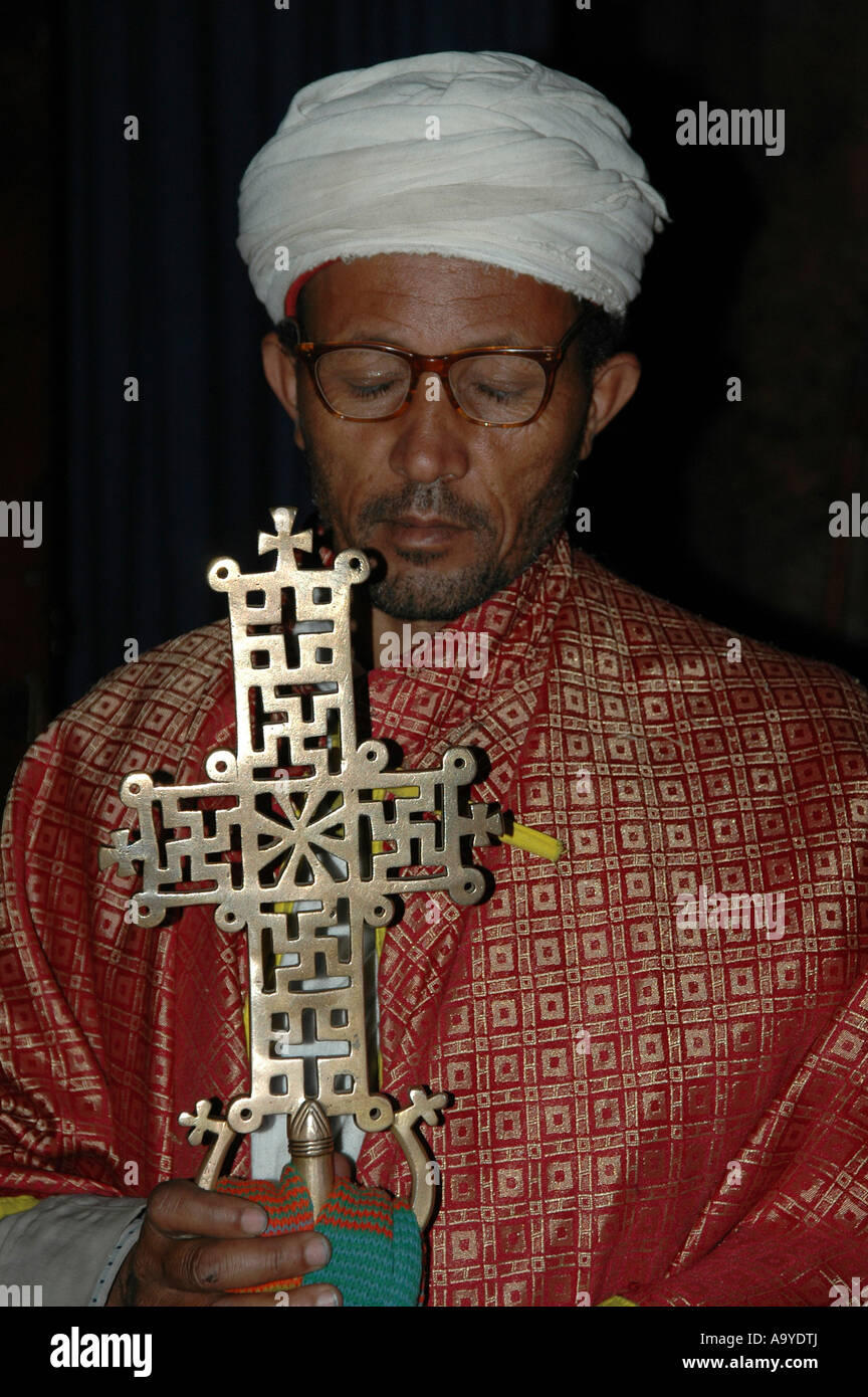 Priest wearing a red cape and a white cap carries artful Lalibela cross rock churches Lalibela Ethiopia Stock Photo