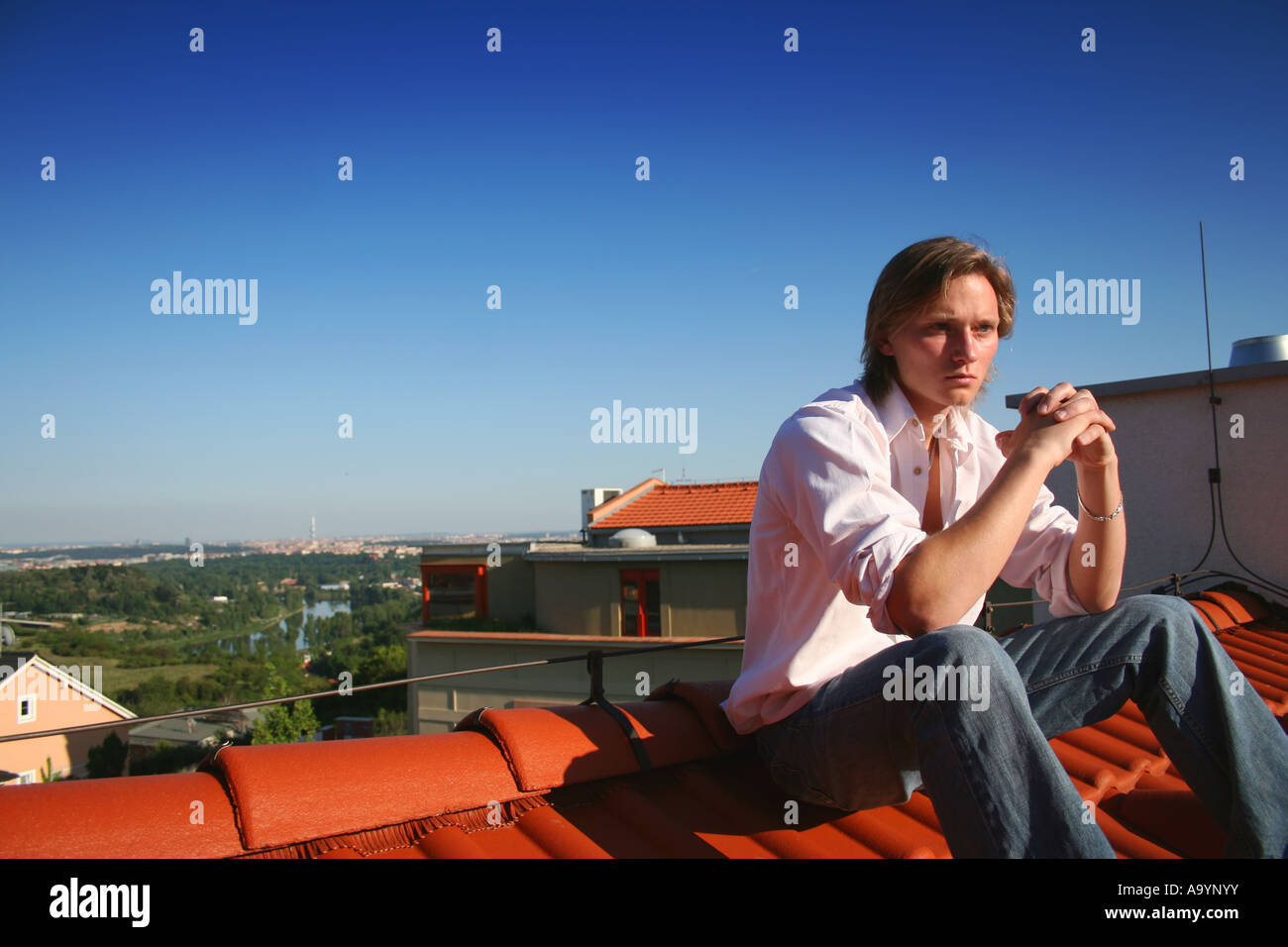 Young person sitting contemplatively on terracotta roof tiles ...