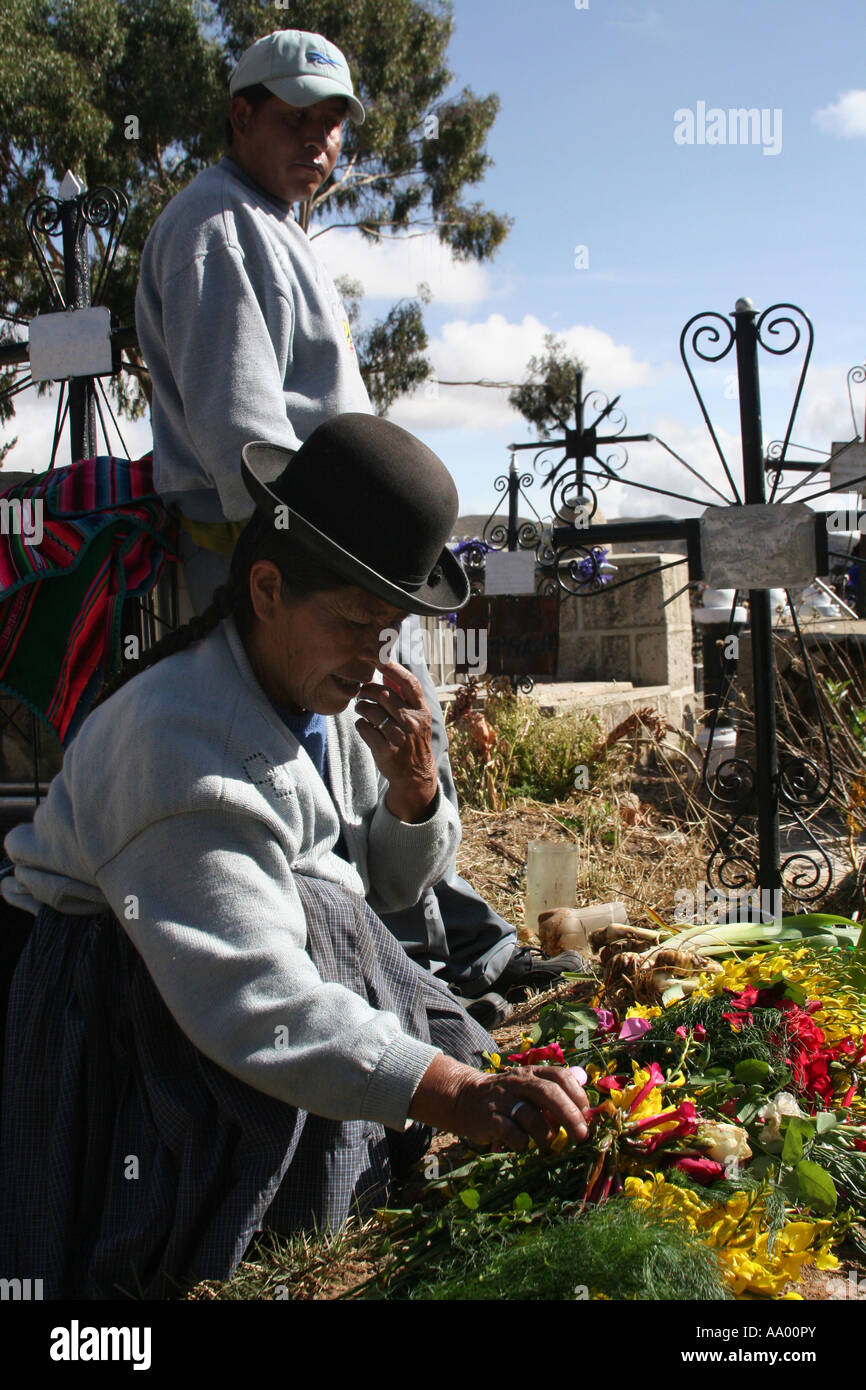 A traditional Bolivian woman in bowler hat and her son at the grave of her husband at All Saints, todos Santos, in Llallagua Stock Photo