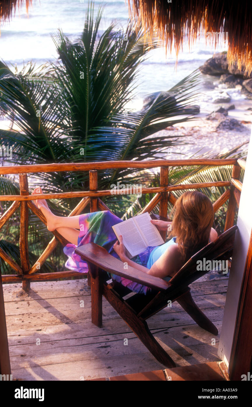 Woman in chair reading with beach and palm trees in the background Tulum Quintana Roo Mexico Model released image Stock Photo