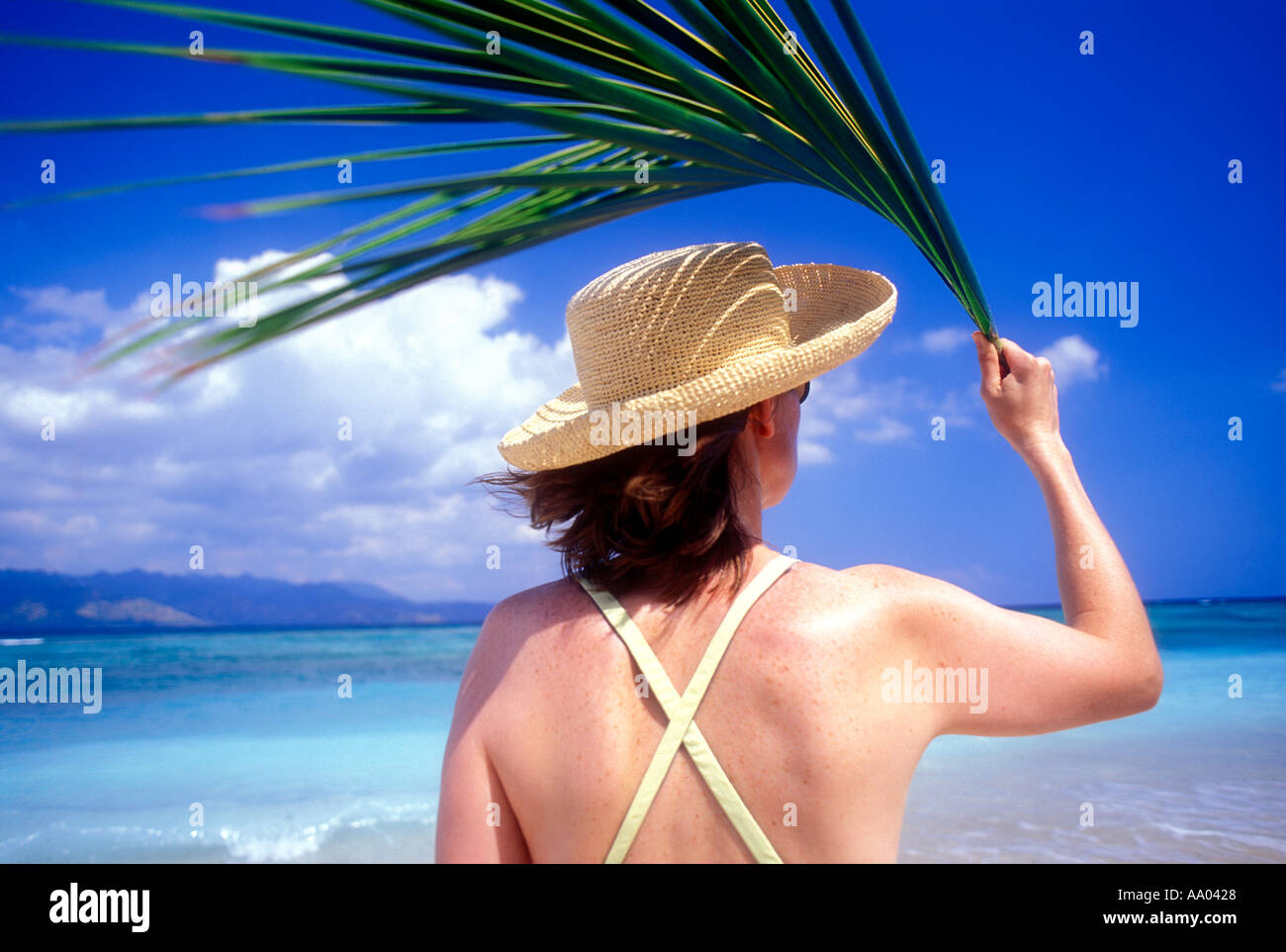 Woman on beach holding palm frond leaf over her head for shade Lombok Island Indonesia Southeast Asia Model released image Stock Photo