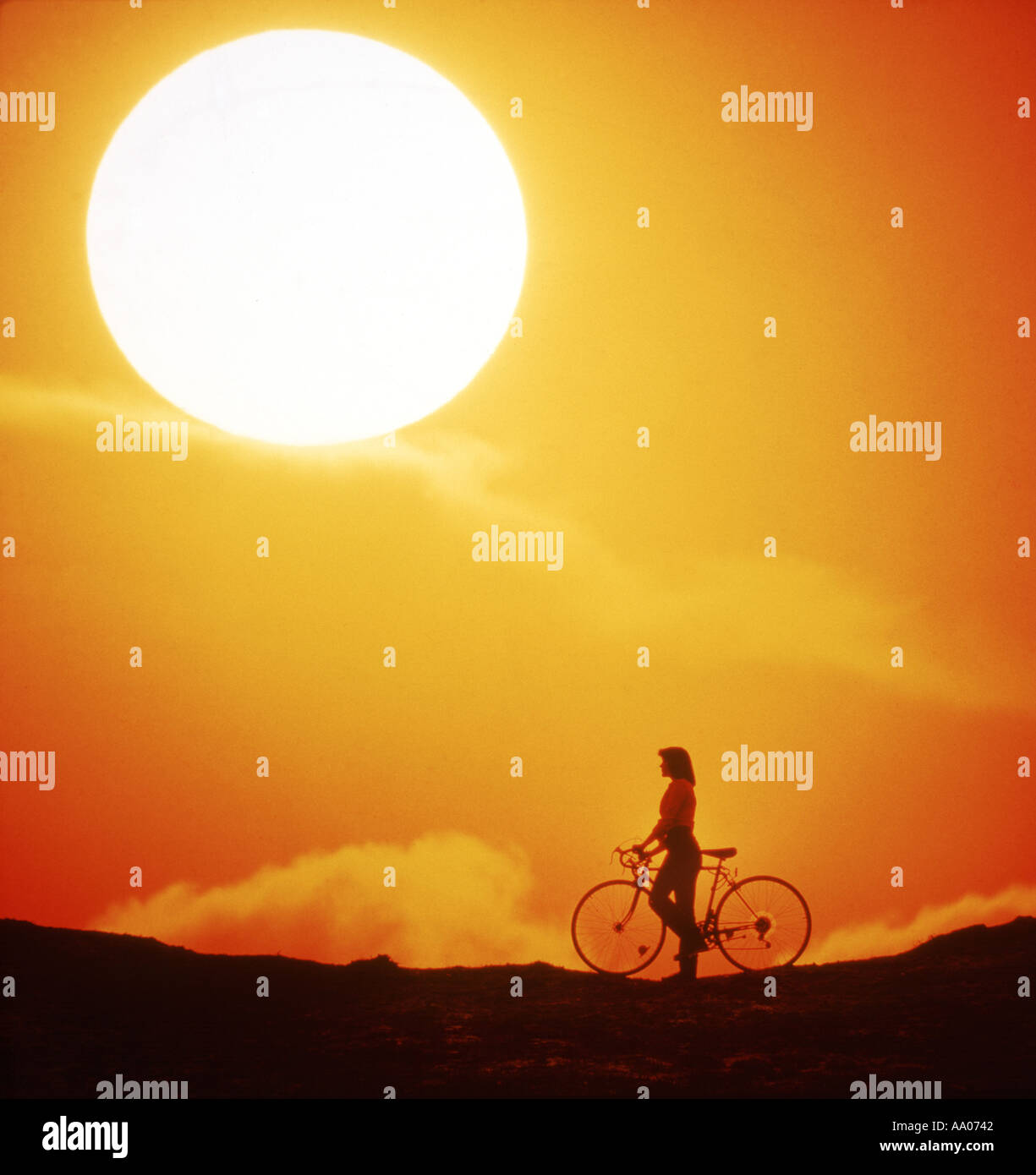 woman pauses beside bicycle to watch huge sunset Stock Photo
